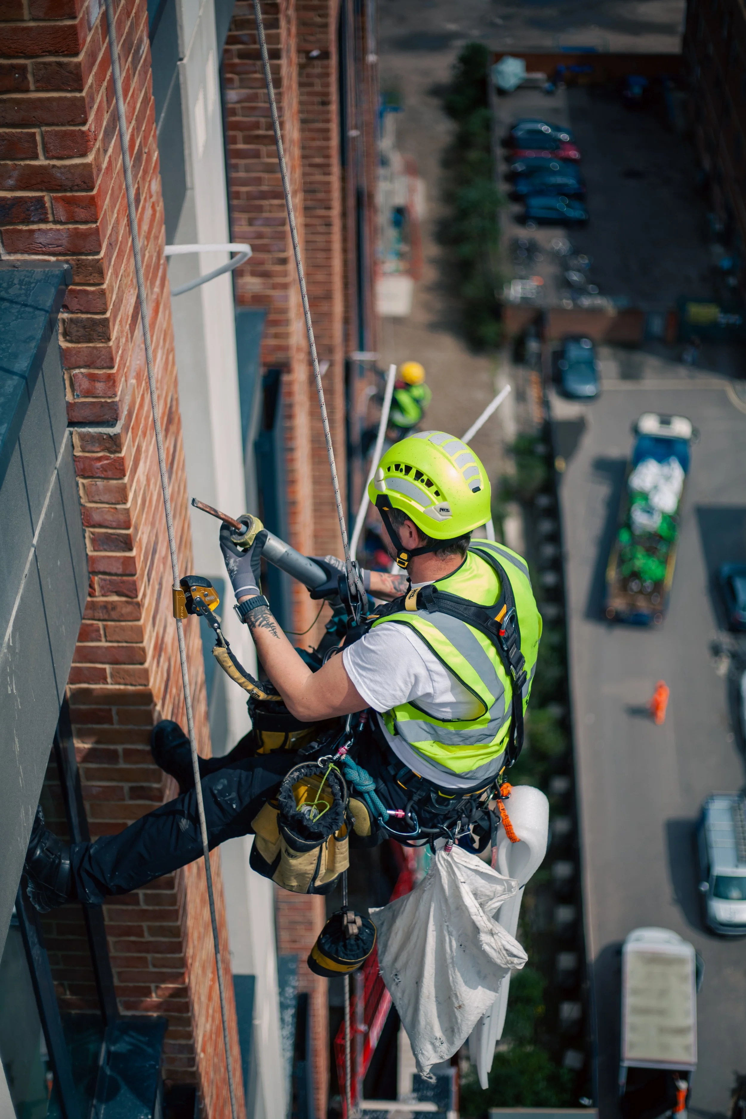 Worker in safety gear performing building maintenance using rope access on a multi-story brick building.