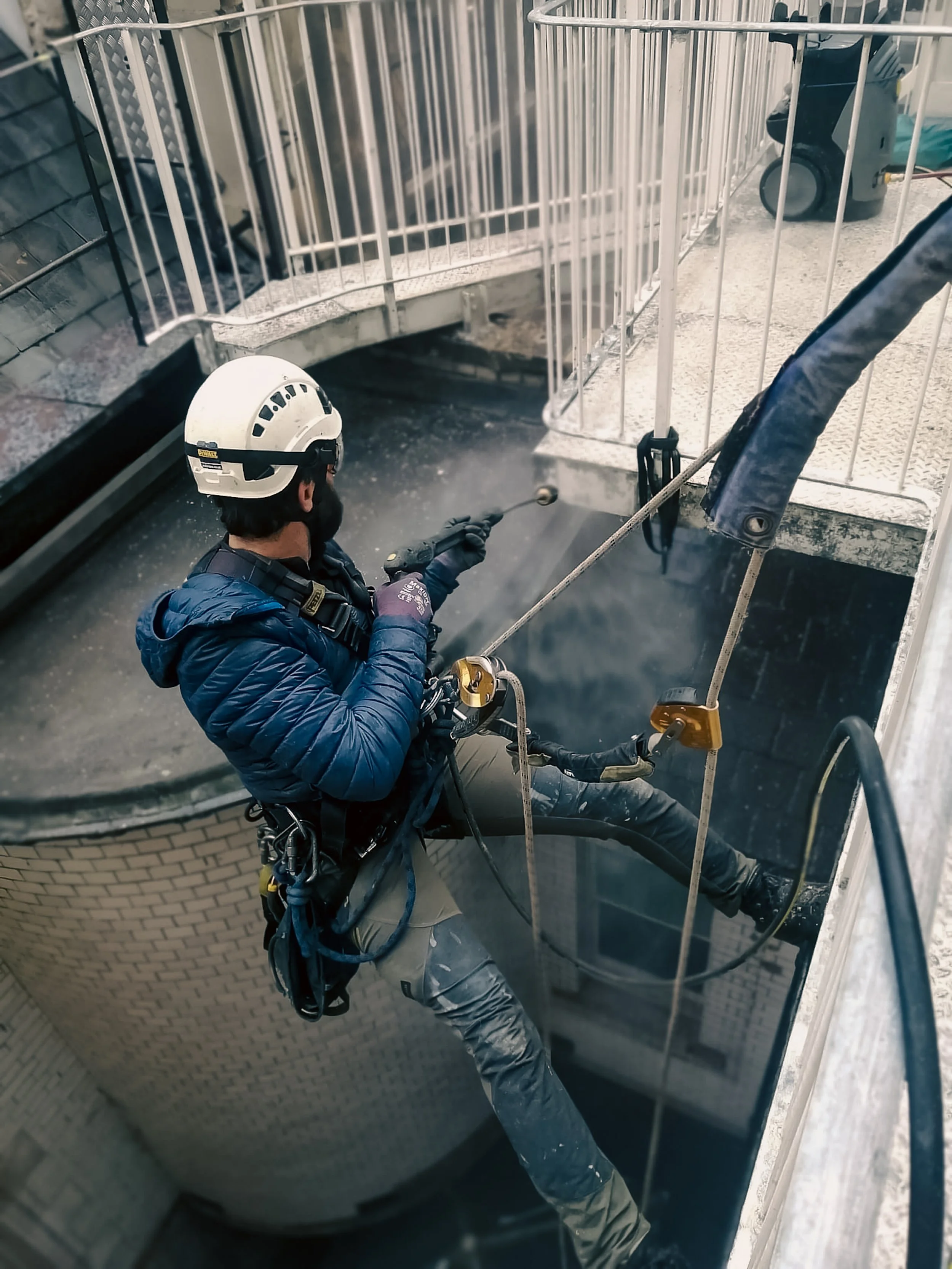 Person in safety gear performing high-rise power washing with harness and ropes