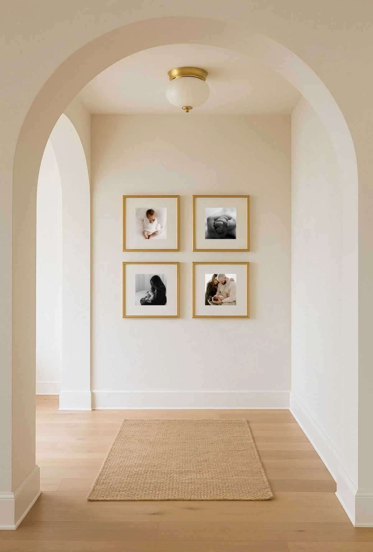 A hallway with a beige carpet, white walls, and four framed black and white photos of babies and a woman with a baby, arranged in a square pattern on the wall.