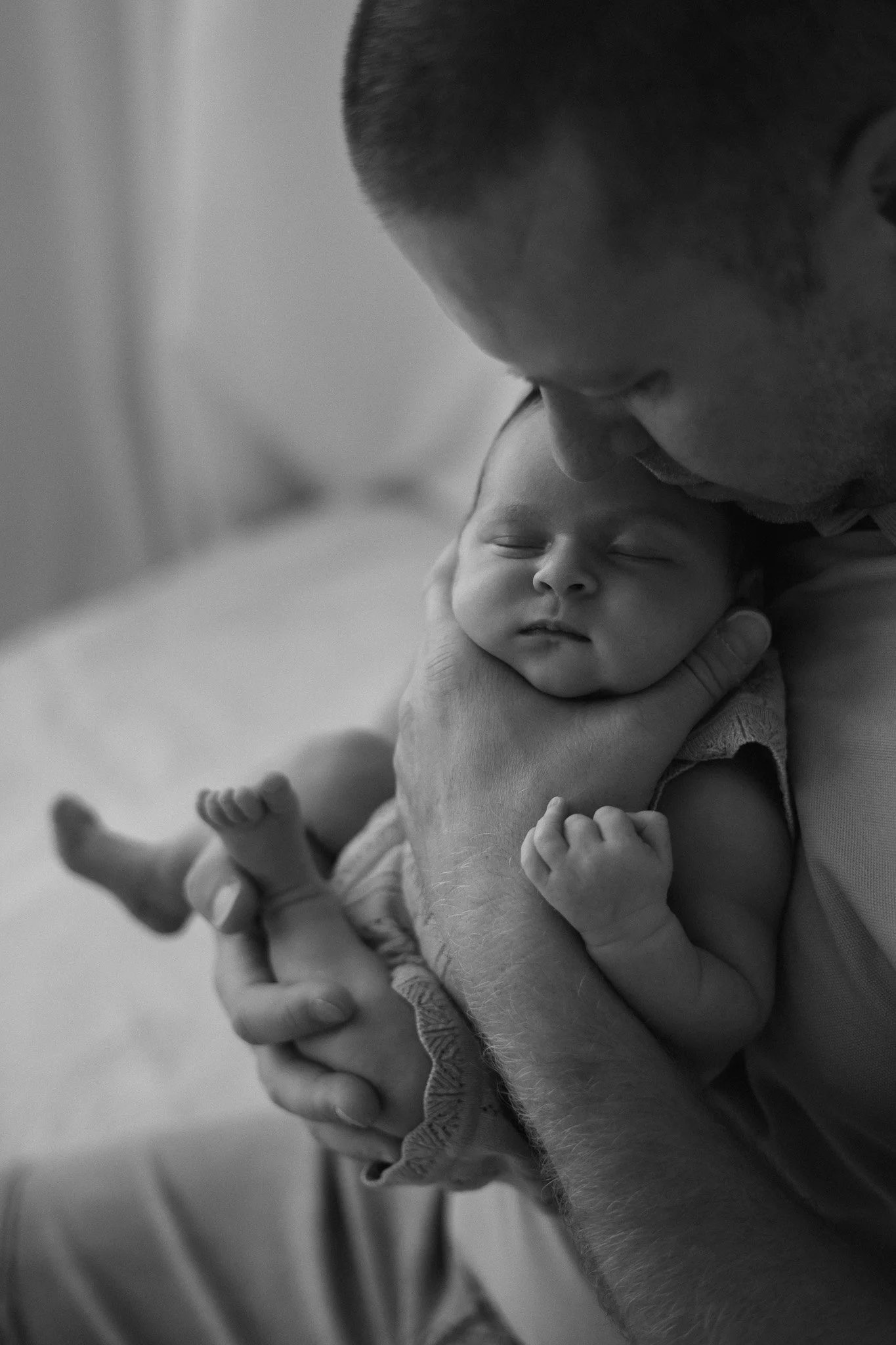 A black and white photo of a man holding a sleeping baby close to his face, gently pressing his forehead to the baby's head.