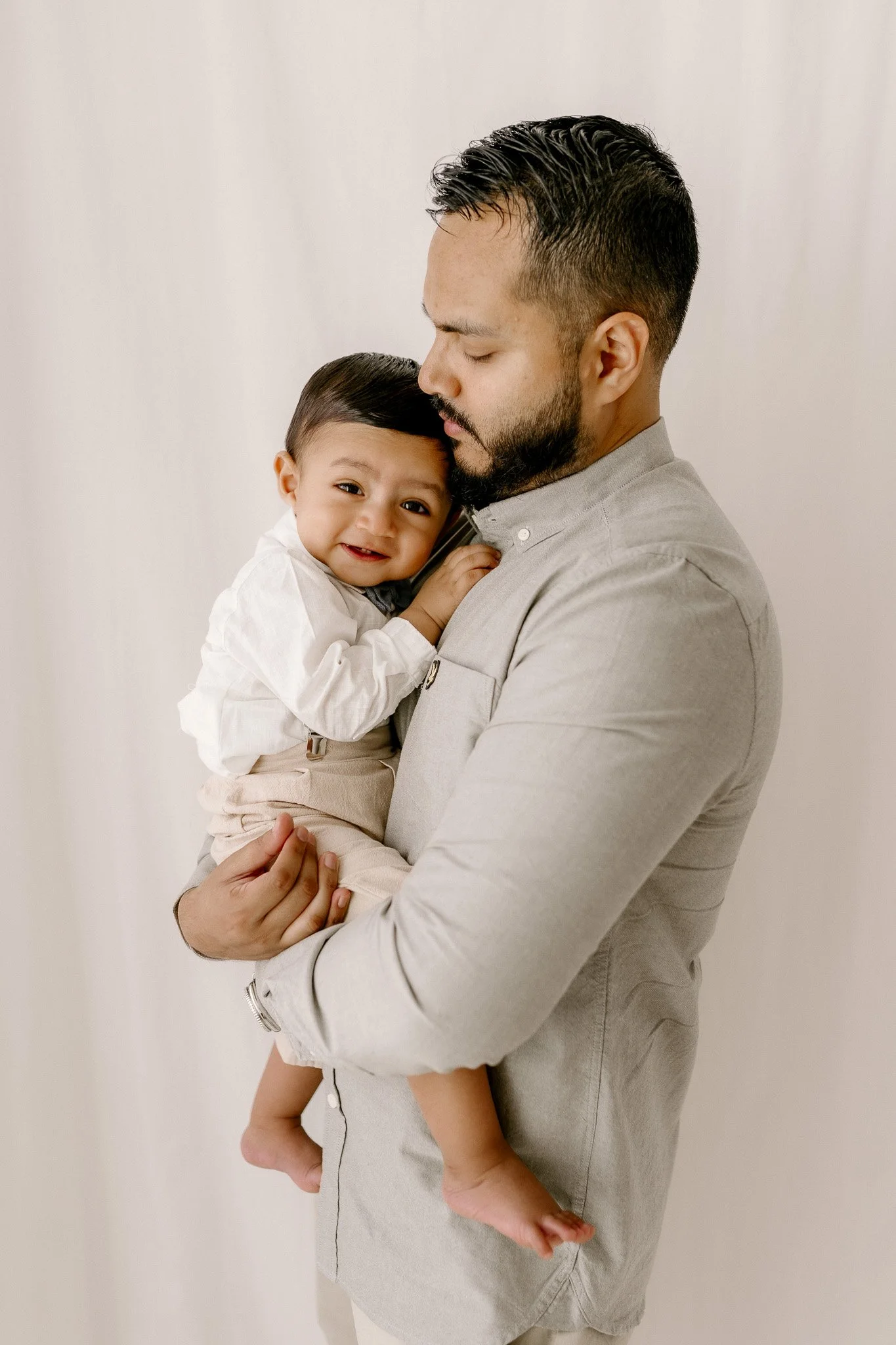 A man holding a young child while standing against a neutral background.