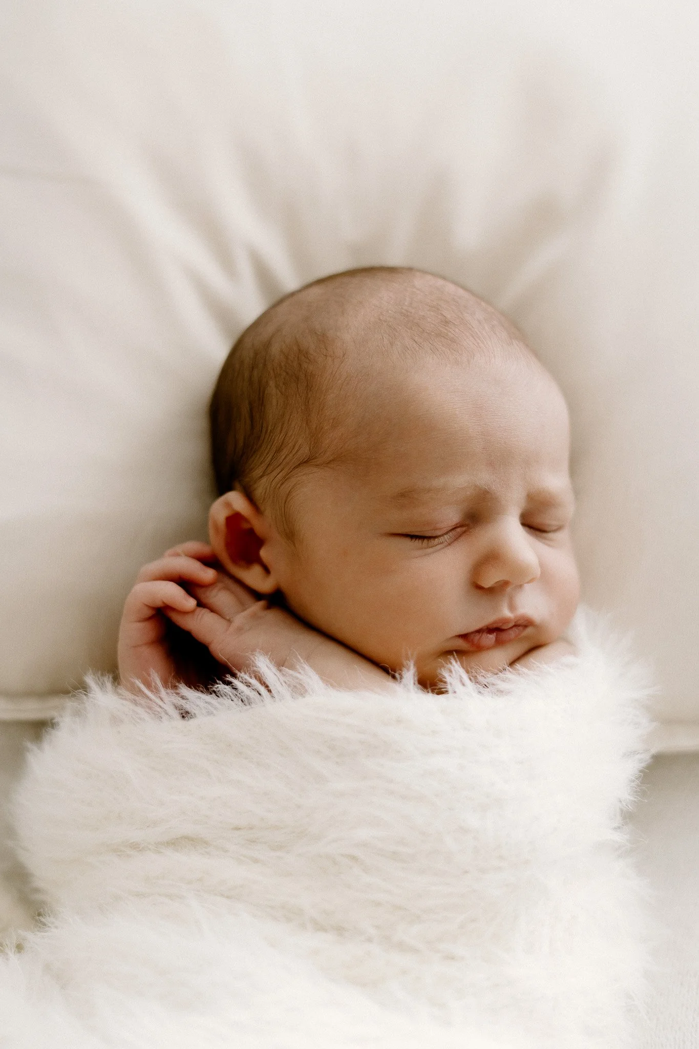 Close-up of a sleeping newborn baby wrapped in a fluffy white blanket.