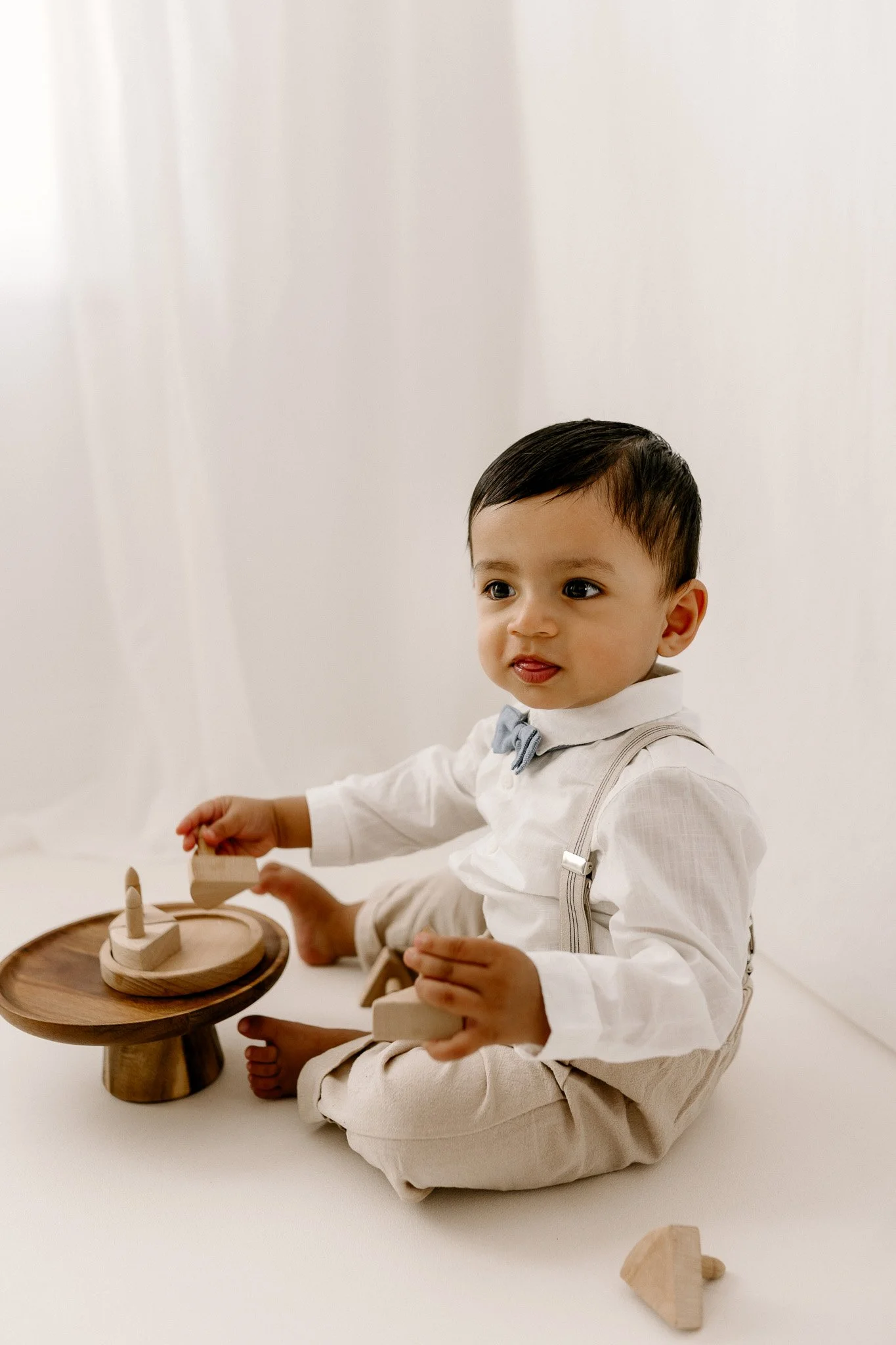Young boy sitting on the floor playing with wooden stacking toys against a white background.