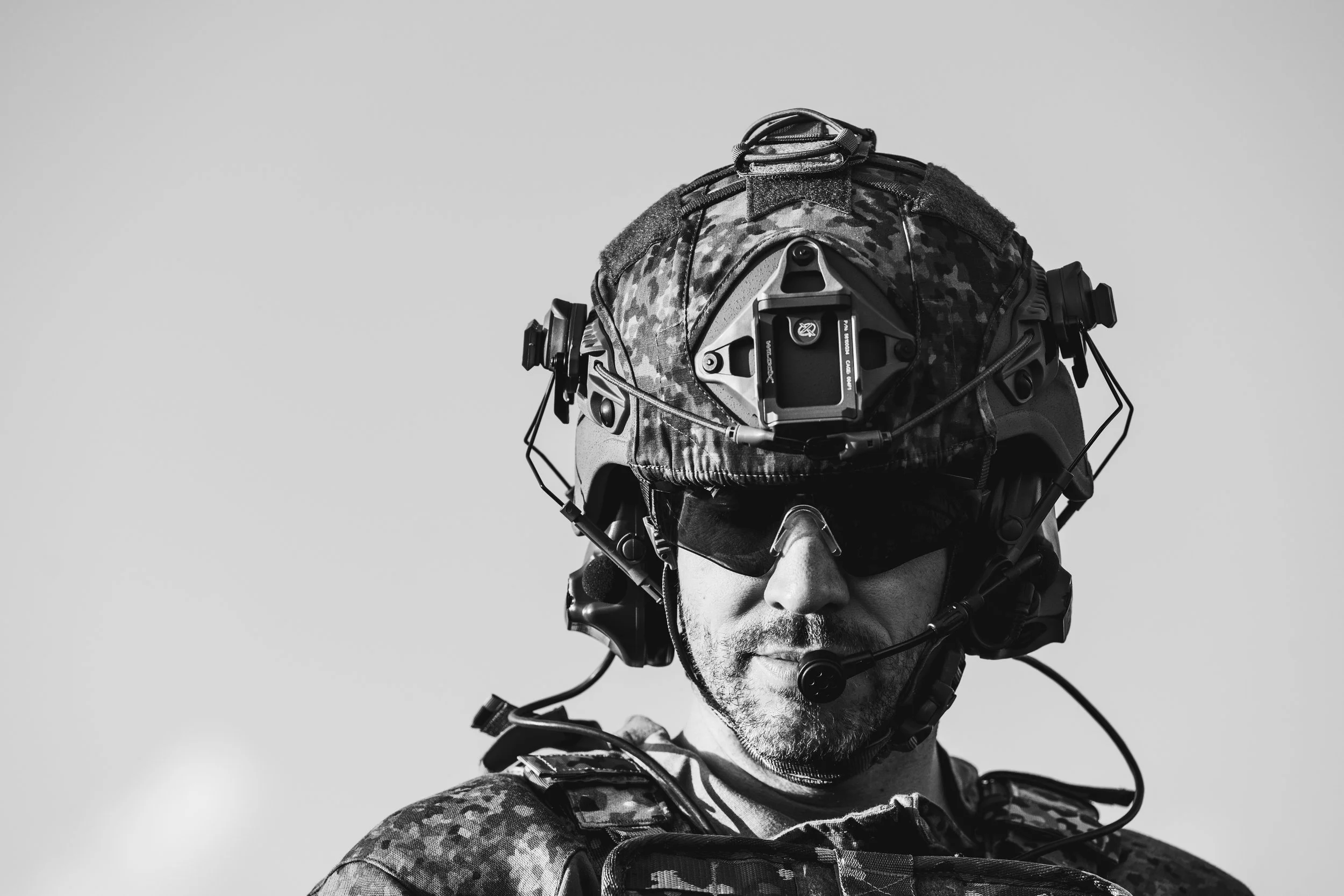 A soldier wearing a military helmet with attached communication equipment and sunglasses.