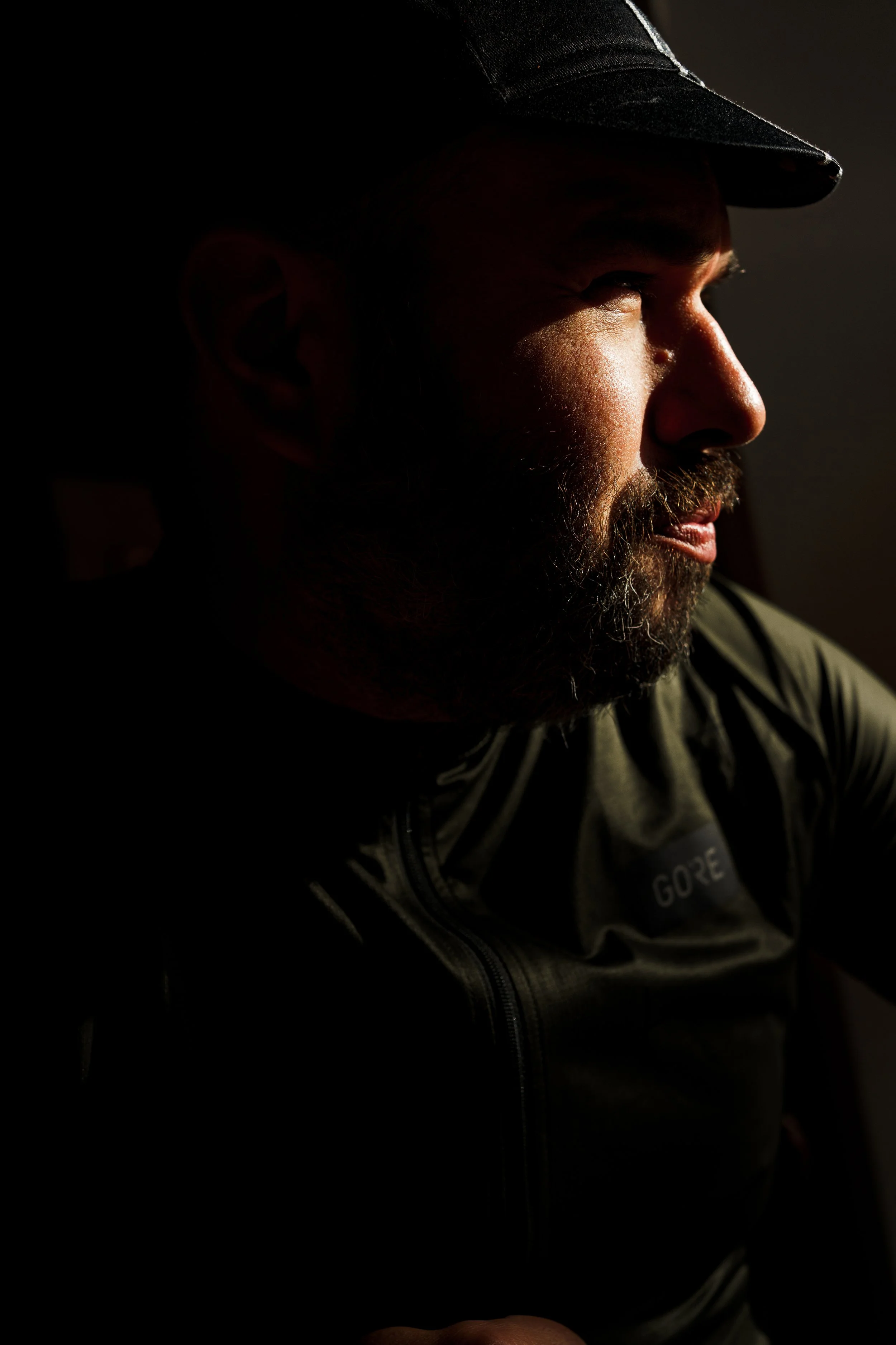 Side profile of a man wearing a cap, with sunlight illuminating his face against a dark background.