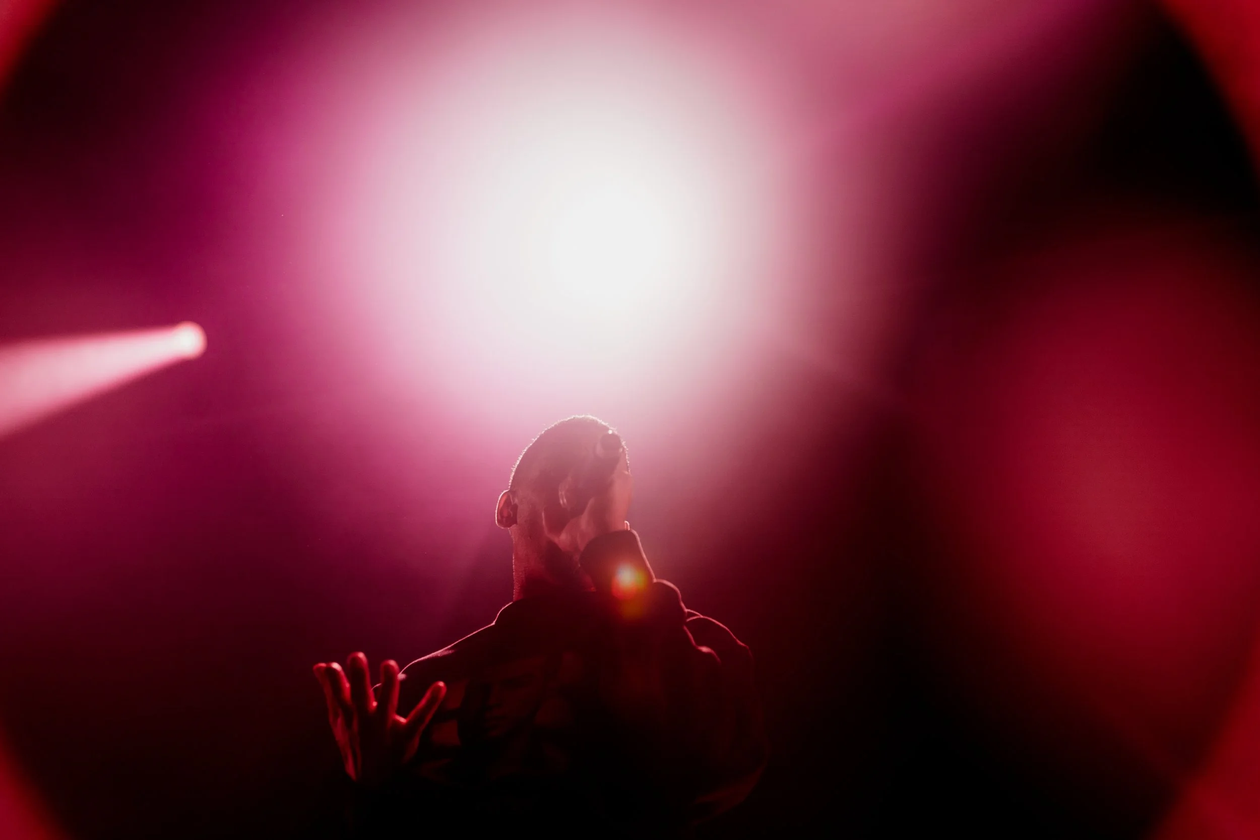 A performer on stage under bright pink and white stage lights, wearing a hoodie with a face printed on it.