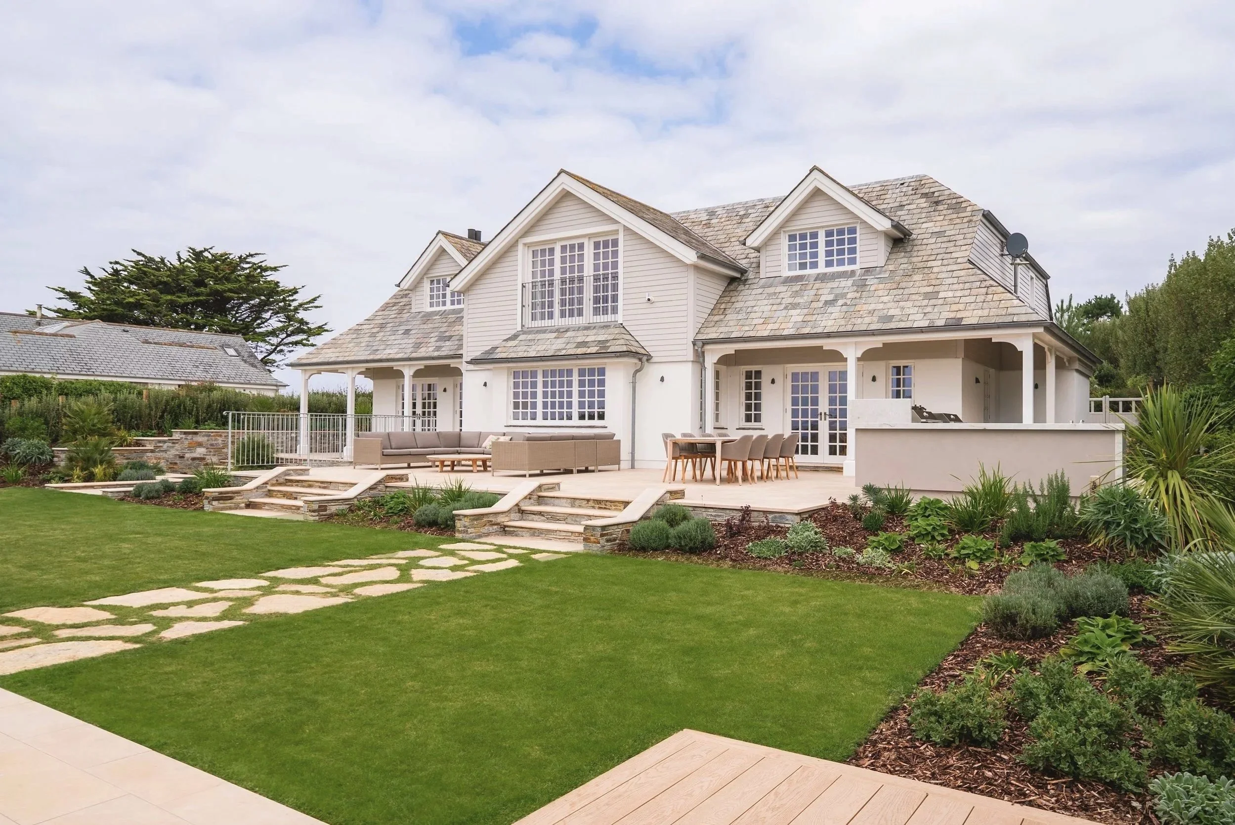 A modern garden design in Rock, Cornwall with a large terrace incorporating an outdoor kitchen, seating area and dining table.