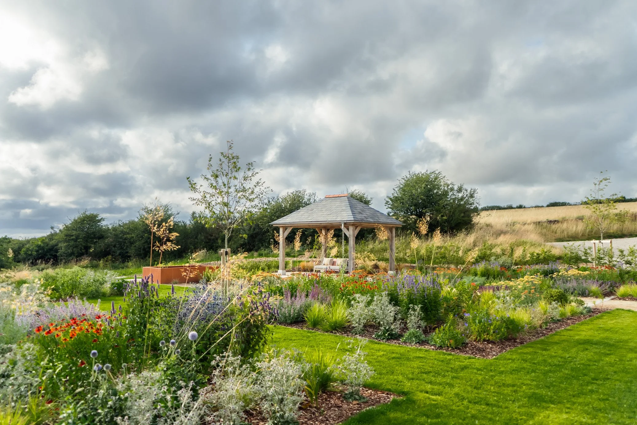 A country garden with a wooden gazebo and outdoor seating area, planted with a colourful wildflower meadow design in Camel Valley, Cornwall
