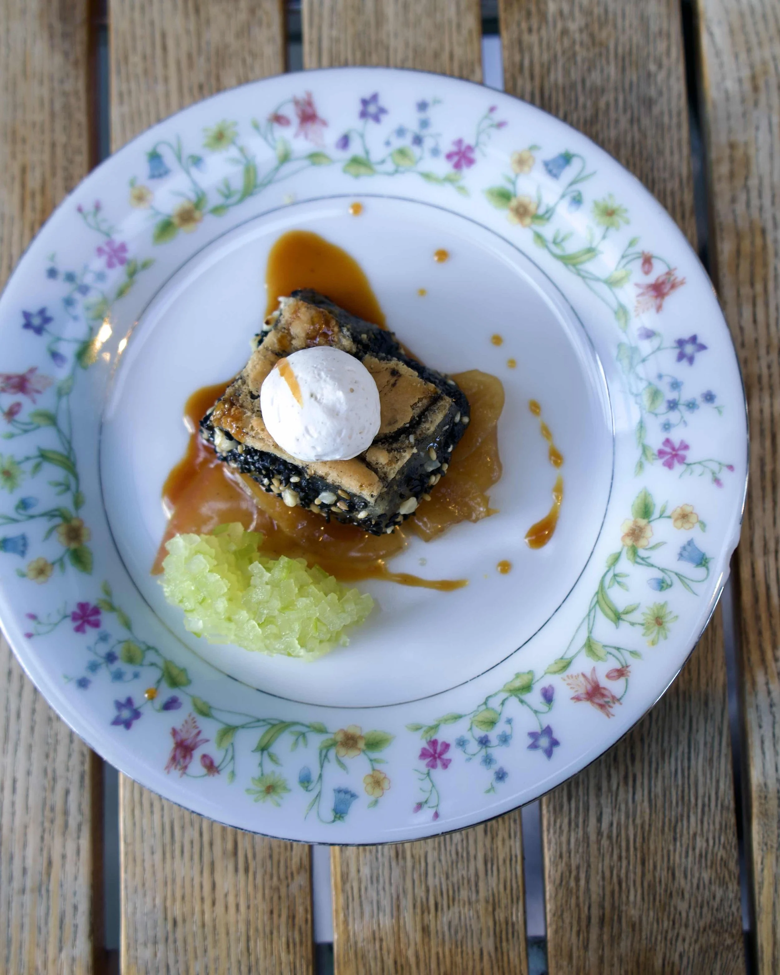 A dessert with a layer of caramelized fruit, topped with a scoop of vanilla ice cream, served on a floral patterned plate placed on a wooden surface.