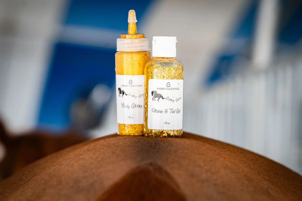 Two bottles of gold-colored glitter labeled 'Armor Equestrian' sitting on a horse's back with a blurred background.