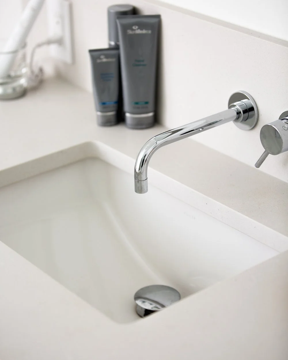 Close-up of a bathroom sink with a chrome faucet, two bottles of shampoo or body wash, and a bar of soap.