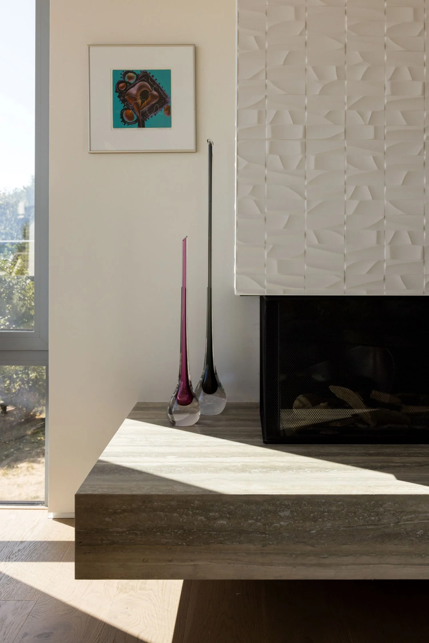 Interior of a modern living room with a fireplace, two tall decorative vases, and a framed abstract artwork on the wall.