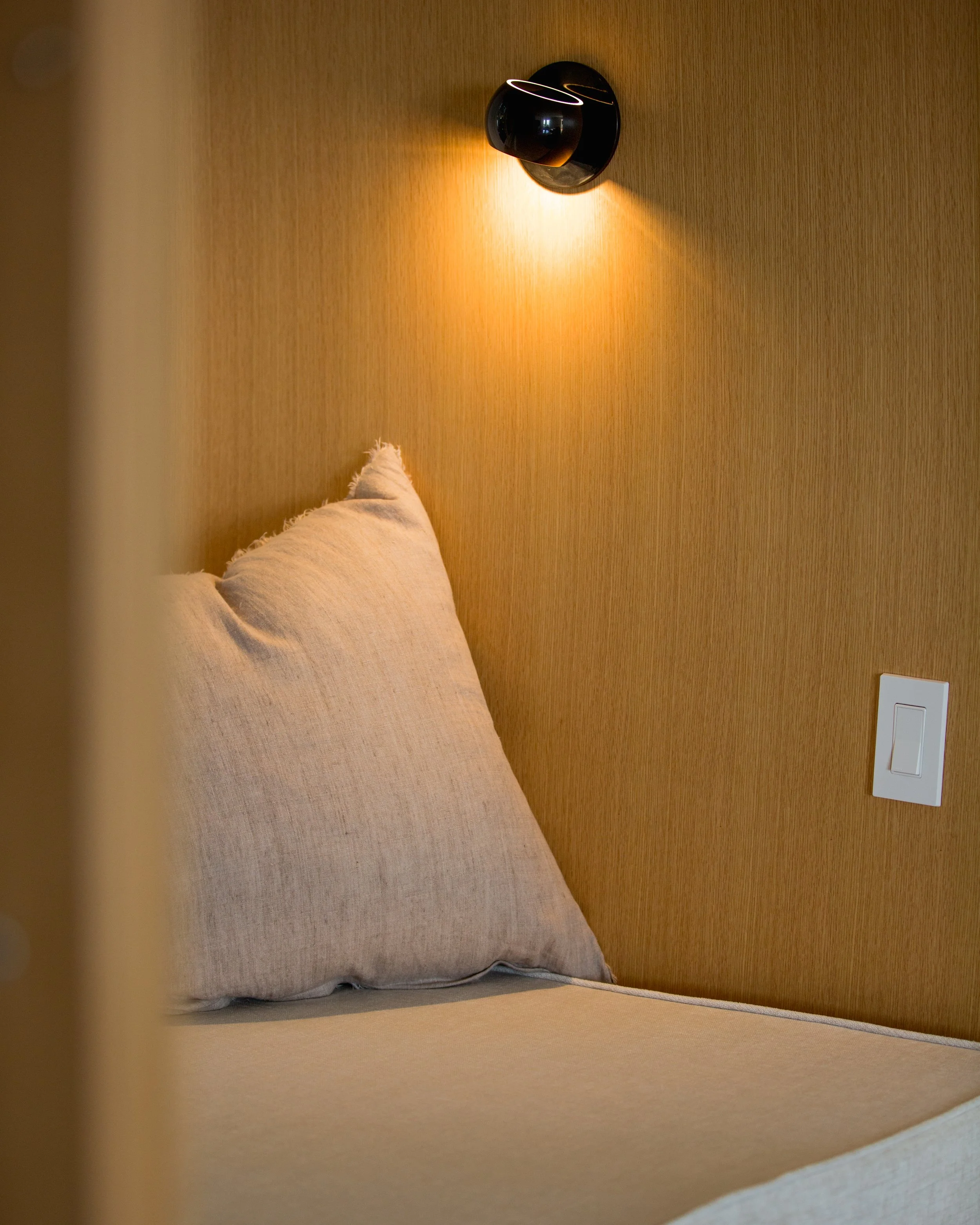 A bedroom corner with a hanging black wall lamp casting warm light.