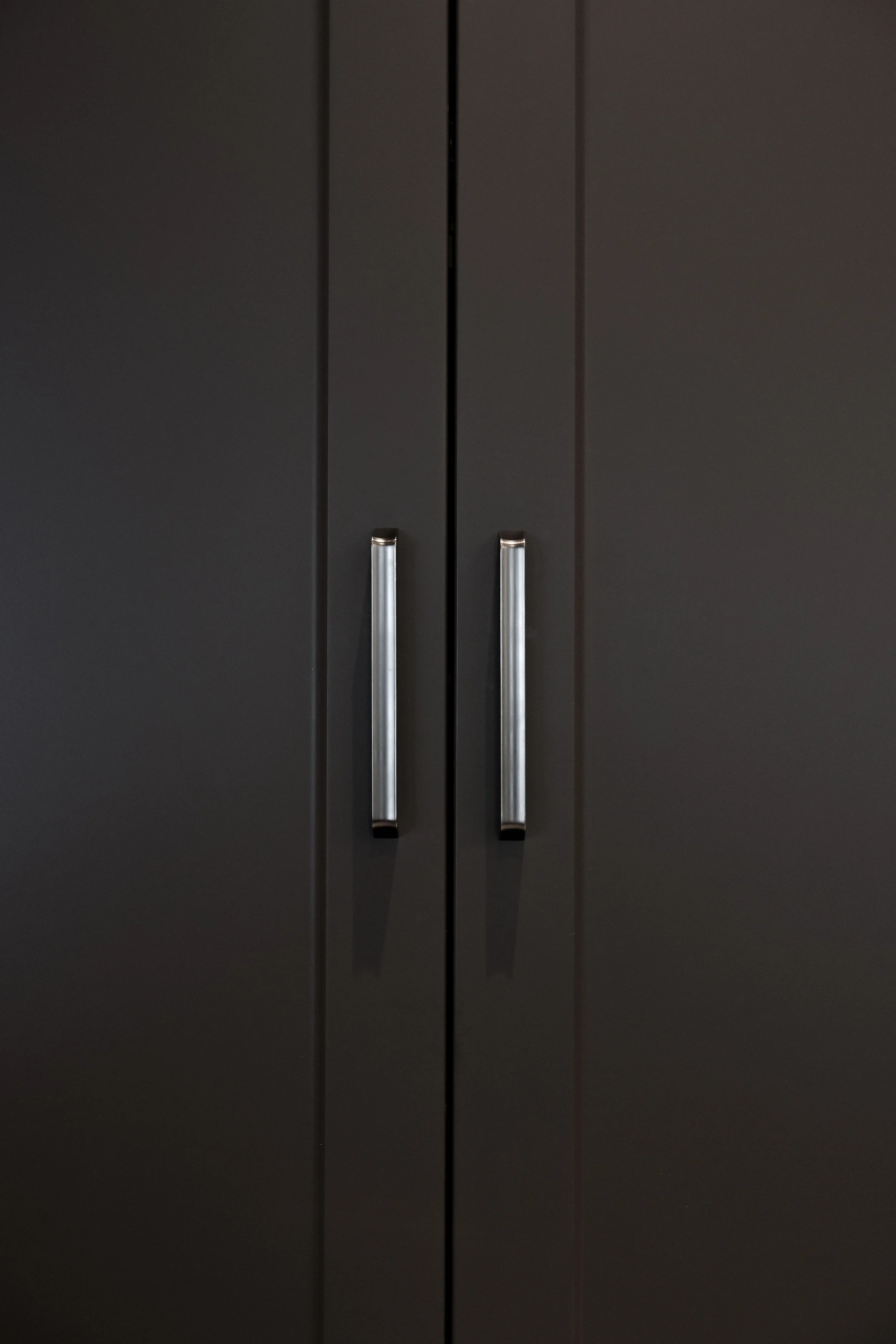 Close-up of a black cabinet with two vertical silver handles.