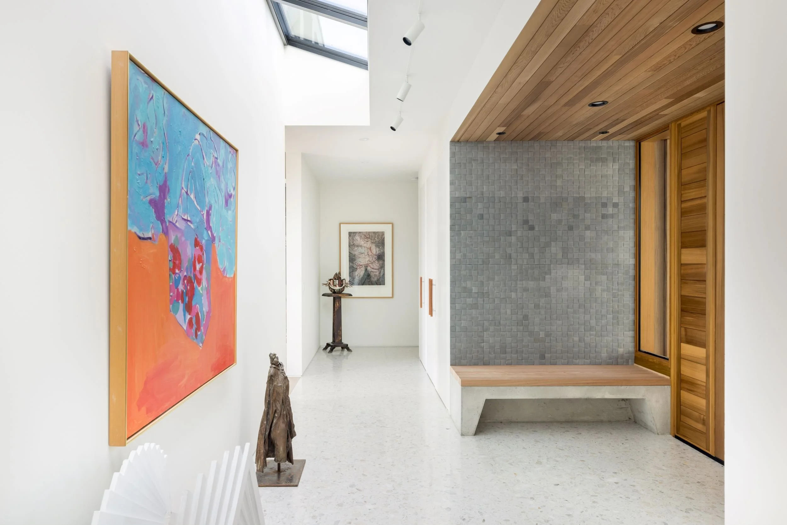 Modern interior hallway with white walls, artwork, stone wall, wooden ceiling, and skylight.