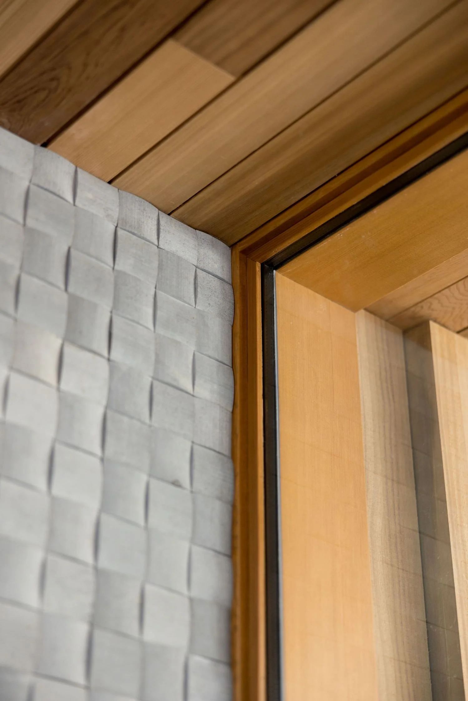 Close-up of a corner showing a wooden ceiling, a wooden window frame, and a textured white wall.