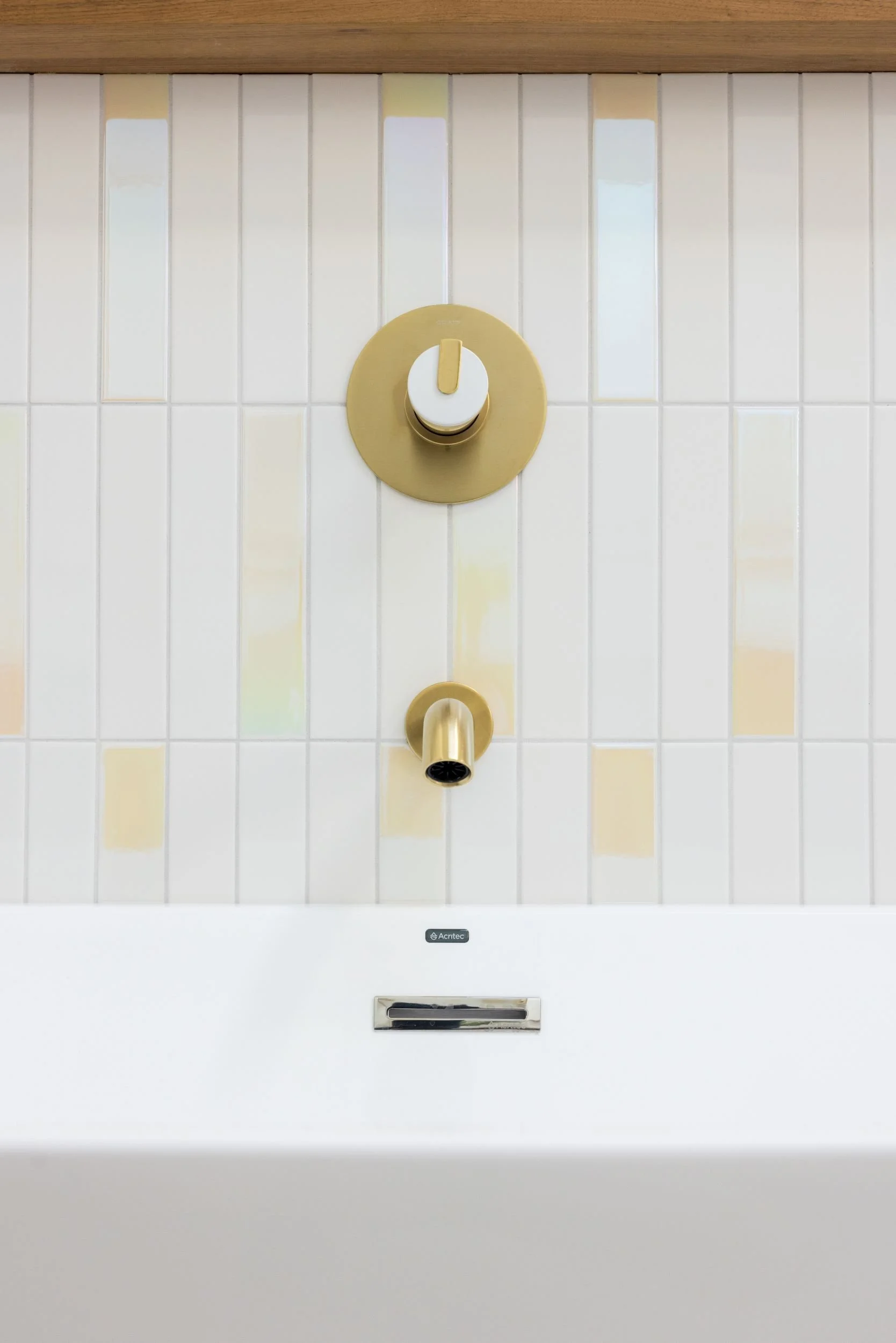 Close-up of a gold wall-mounted faucet with a round control knob above, on a tiled wall, and a white basin below.