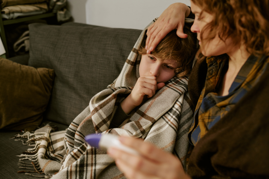 Parent comforting a sick child wrapped in a blanket while checking their temperature at home