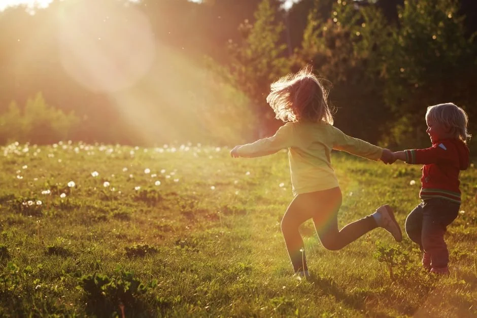 two kids running in a field of dandelions with the sun shining through casting golden light