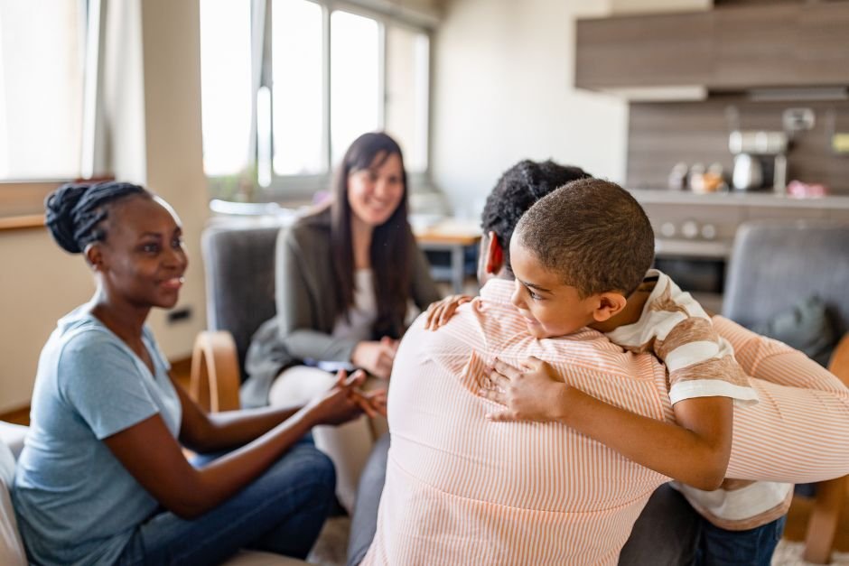 A child hugging his father with the mother smiling at them and the therapist smiling at them