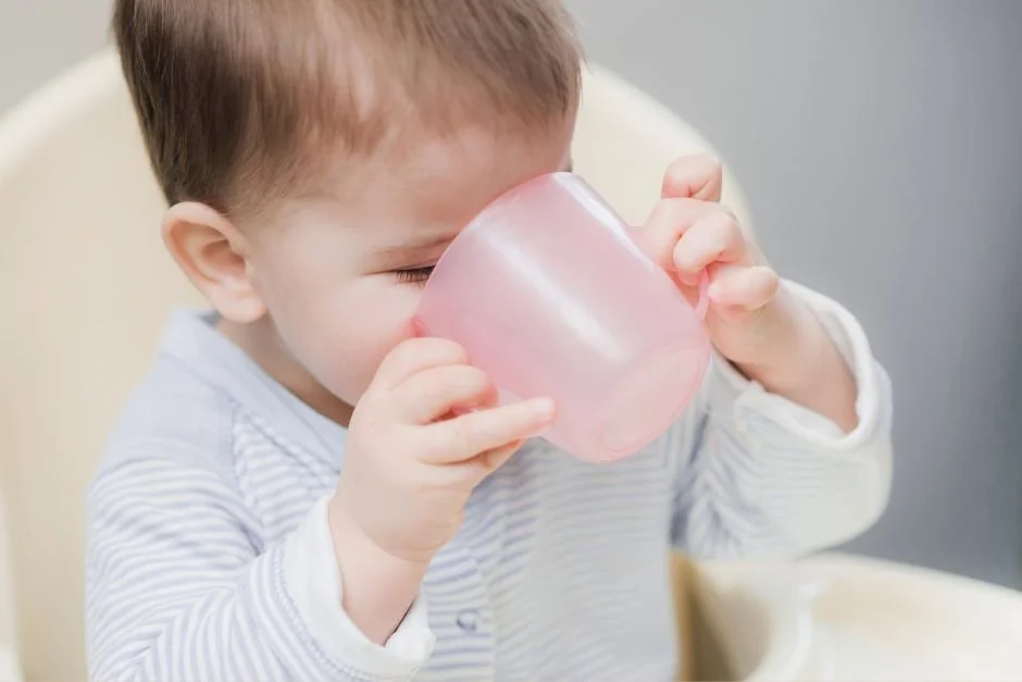 Little boy drinking out of an open cup from a highchair