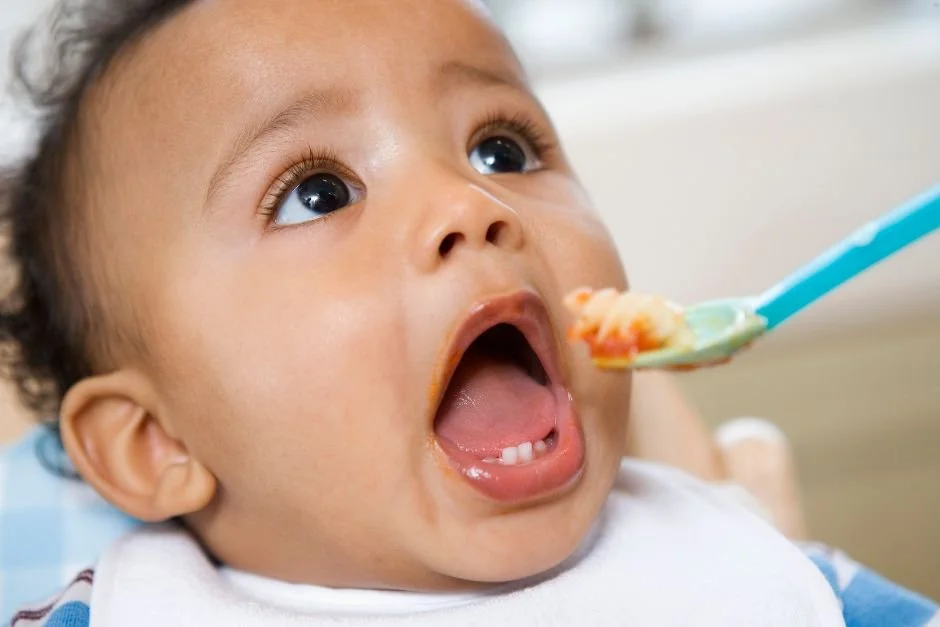 Baby opening their mouth as a spoonful of soft food is offered during feeding.