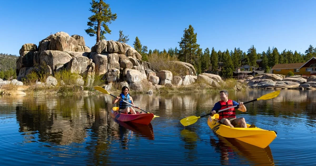 Woman and man paddling in kayaks across a serene summer mountain lake.