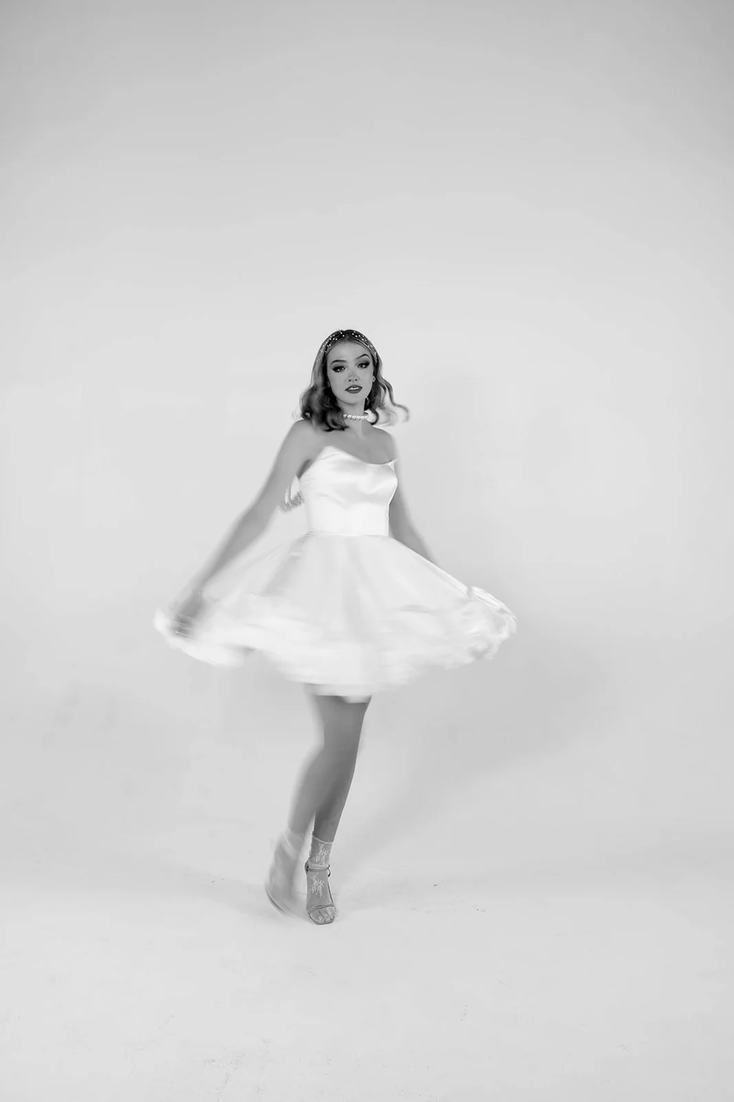 Bride twirling in a short satin wedding reception dress during a studio photoshoot, showing movement and modern bridal style.