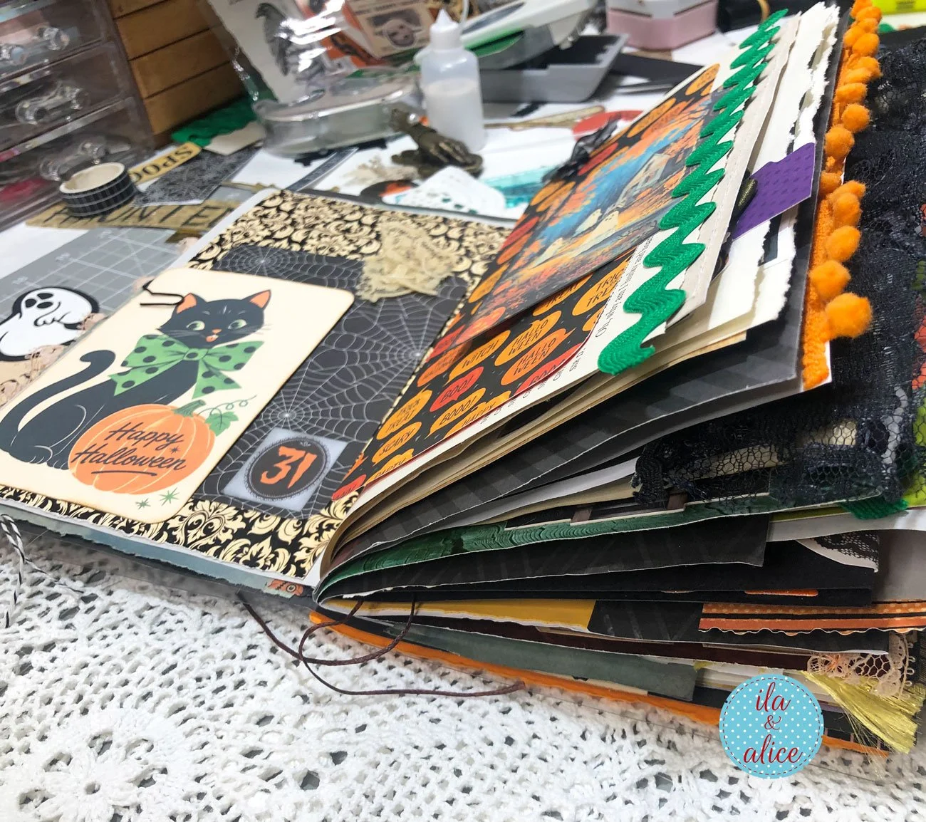 Side view of an overstuffed black and orange Halloween junk journal with black cats, ghosts, layered papers, lace and colourful trims