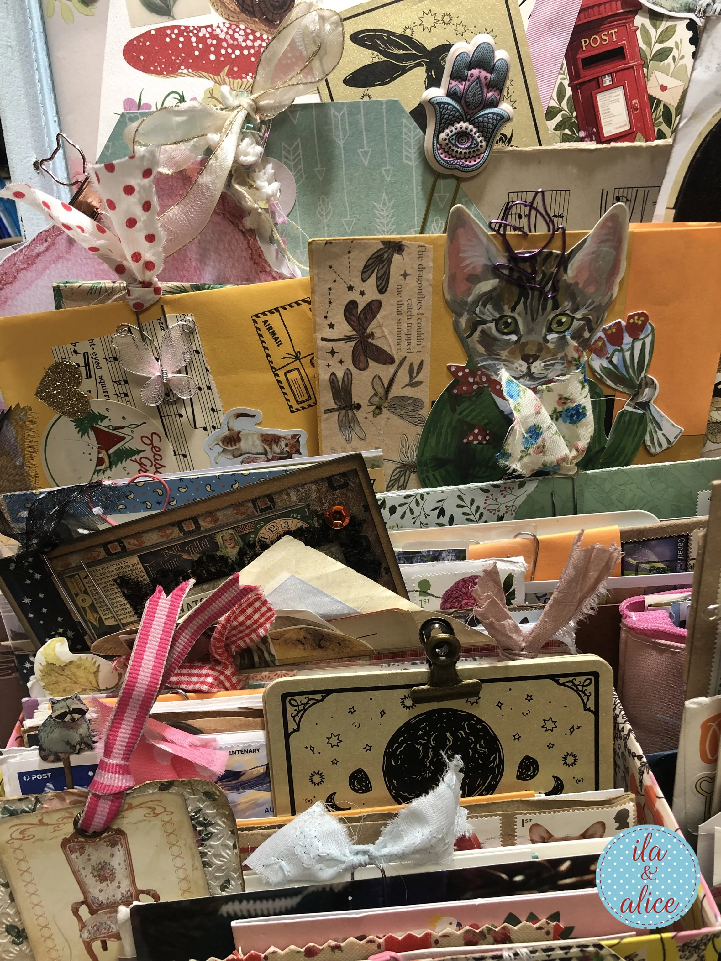 Detailed view of a happy mail archive with a handmade cat card, moon card, ribbon tags, envelopes, botanical paper pieces, and layered ephemera in a vintage suitcase.