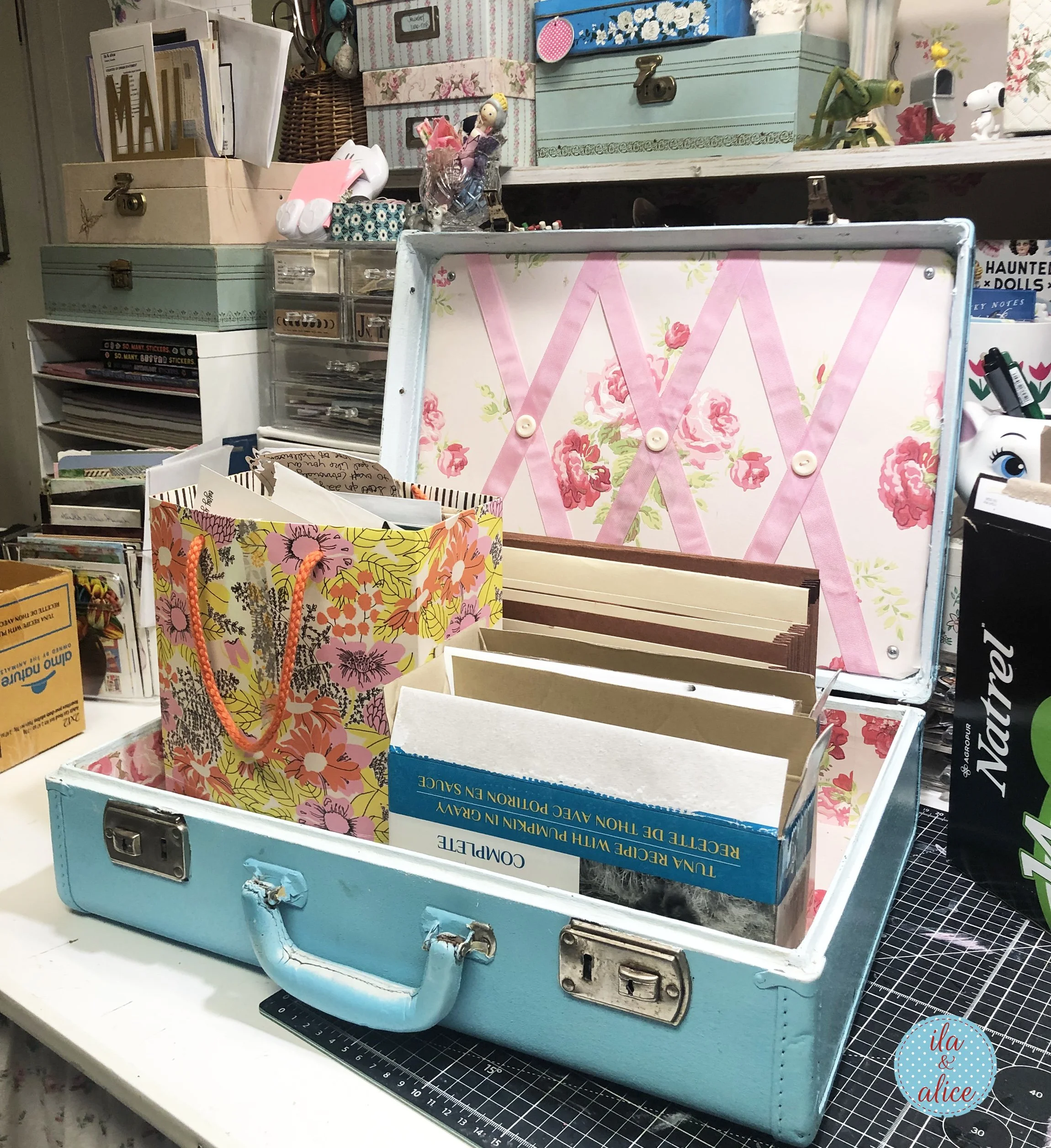 Vintage blue suitcase on a craft desk with floral boxes, cardboard dividers, and paper storage sections being prepared for happy mail organization.