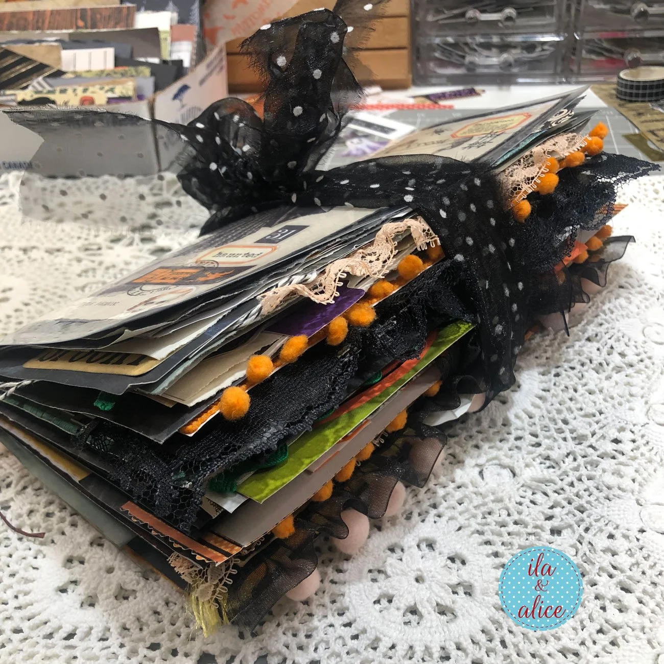 Side view of a very chunky handmade Halloween junk journal filled with lace, orange pompom trim and layered pages, tied with black spotted ribbon