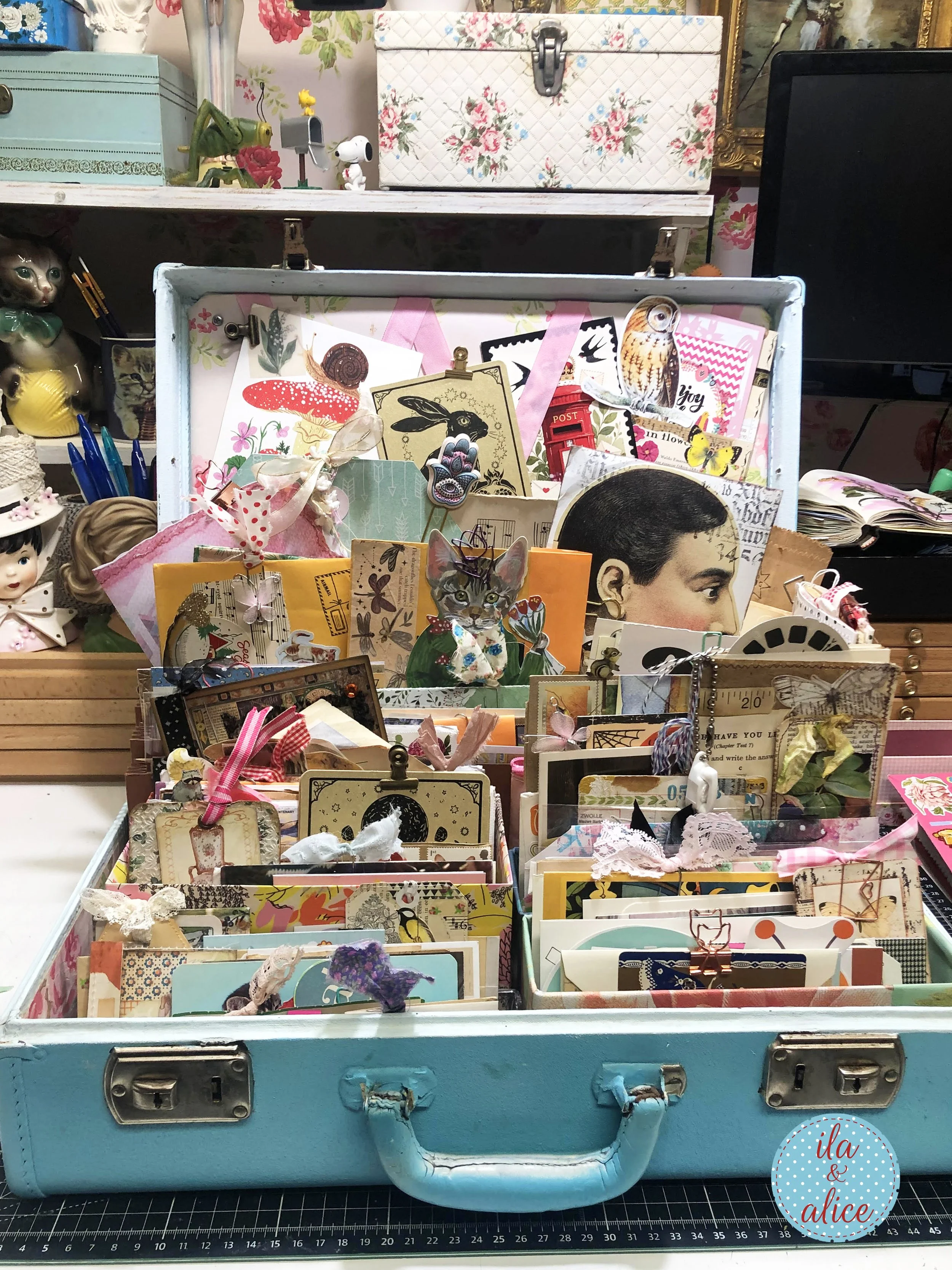 Vintage blue suitcase on a craft desk, organized with years of happy mail, postcards, cards, handmade paper pieces, tags, and envelopes.