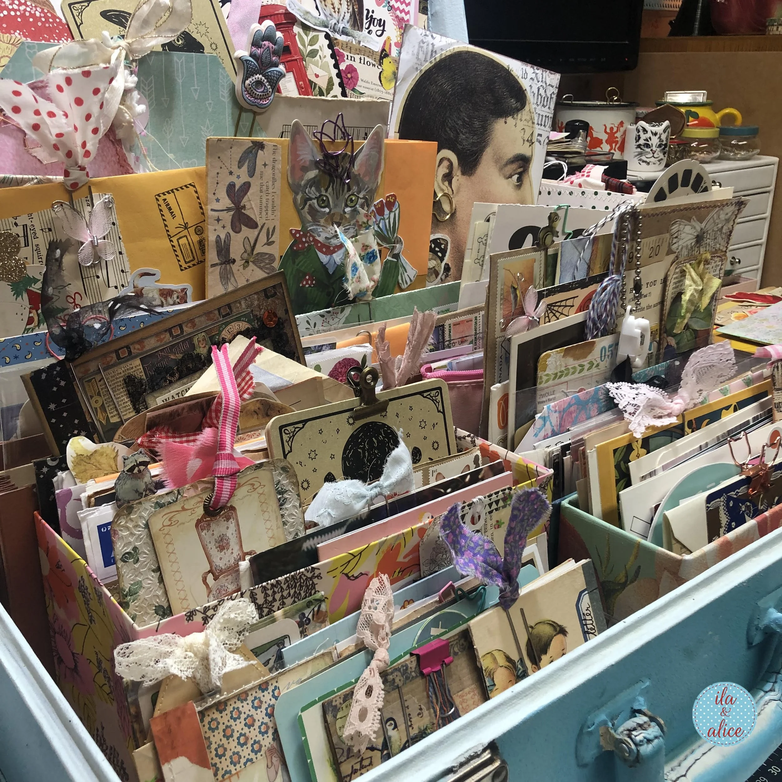 Close-up of a vintage blue suitcase filled with organized happy mail, postcards, handmade tags, envelopes, lace, clips, and paper ephemera.