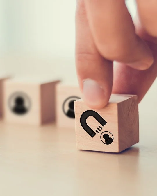 A hand holding a wooden block with a magnet and a ball illustration, with more blocks in the background.