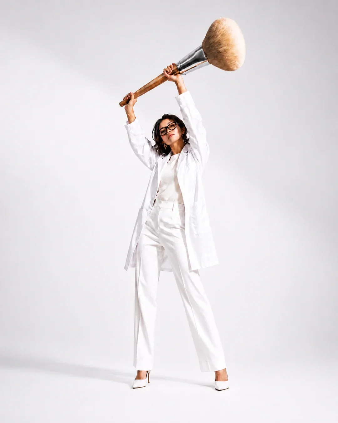 Editorial image of a woman in white holding an oversized makeup brush, representing MMNine Lab’s makeup booking services for events, occasions, photoshoots, and creative projects.