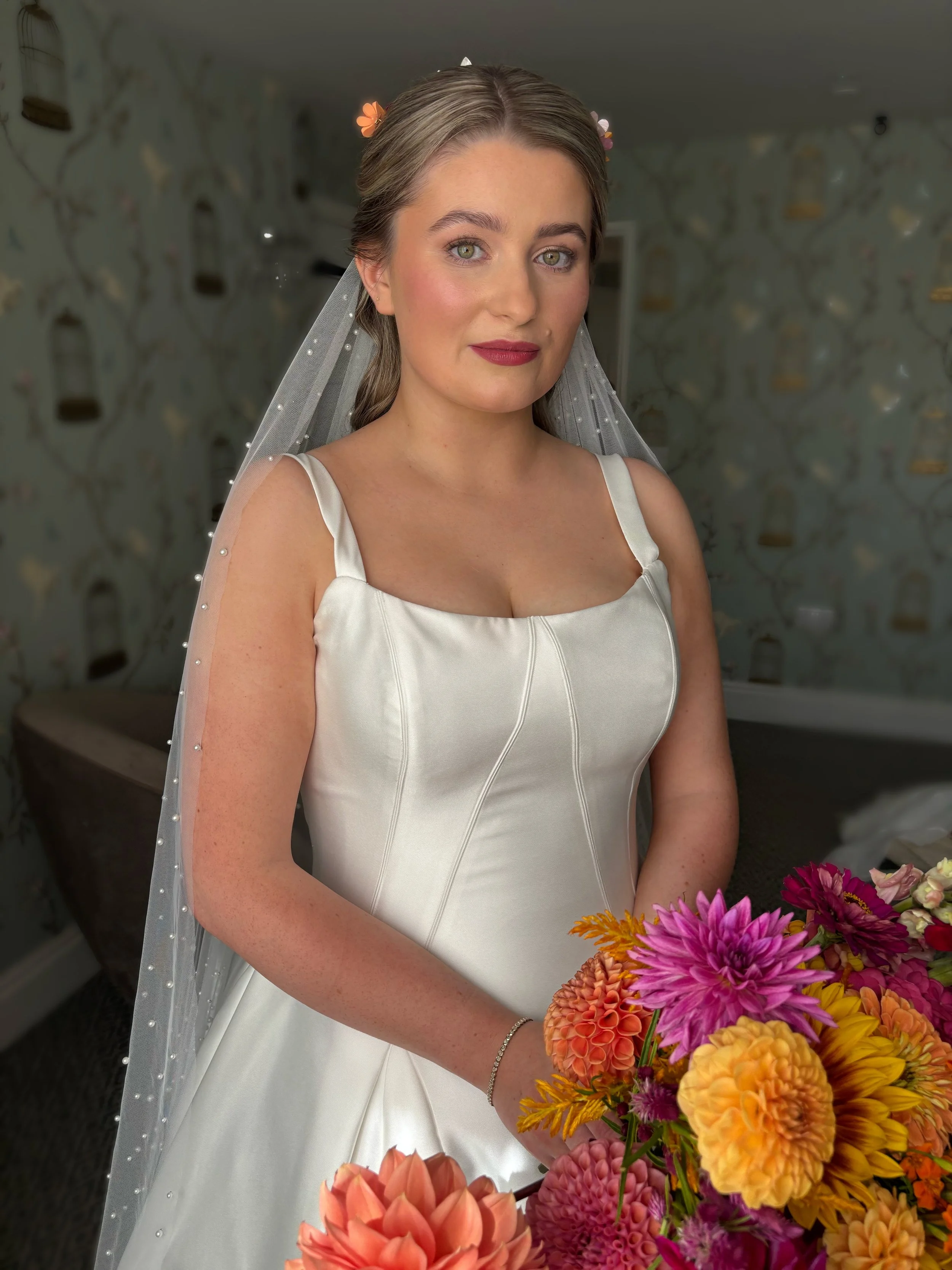 Young woman with light brown hair wearing a tiara and navy blue spaghetti strap top looking at herself in a mirror.