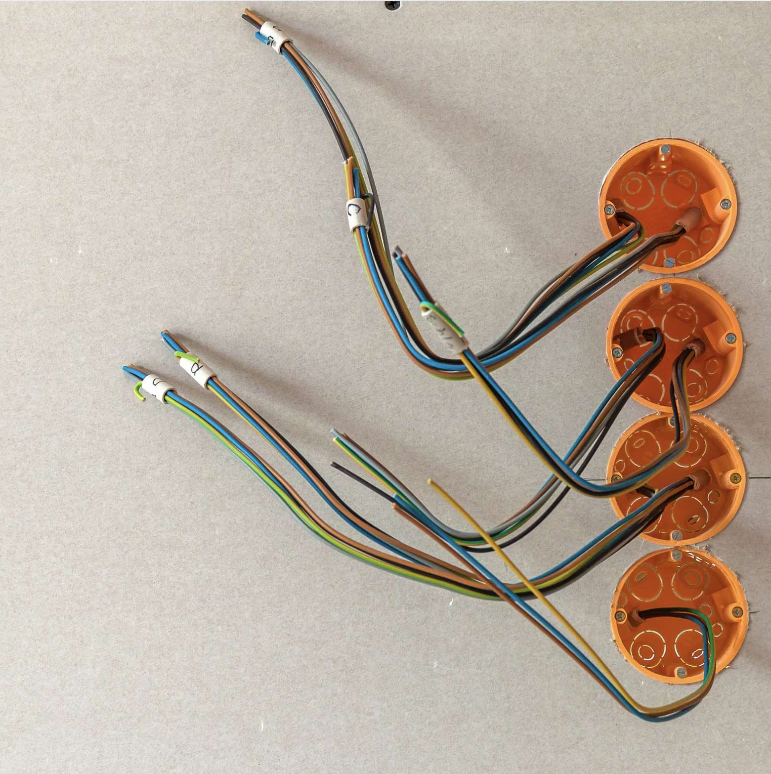 Mehrere miteinander verbundene elektrische Kabel in orange Kunststoffgehäusen auf einer hellgrauen Oberfläche.