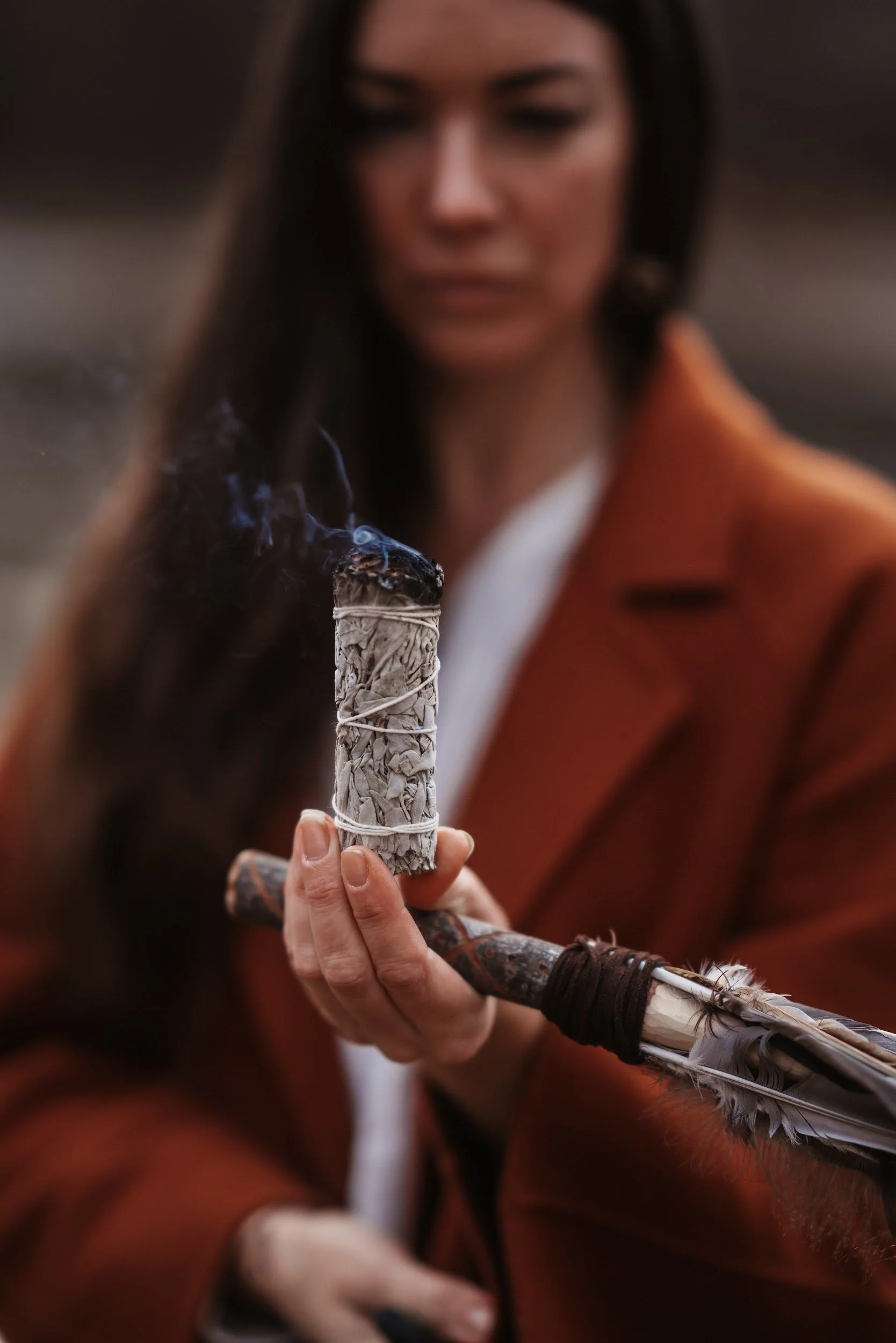 Frau mit brauner Jacke hält eine zeremonielle Rauchfeder, die auf einer langen Pfeife montiert ist.