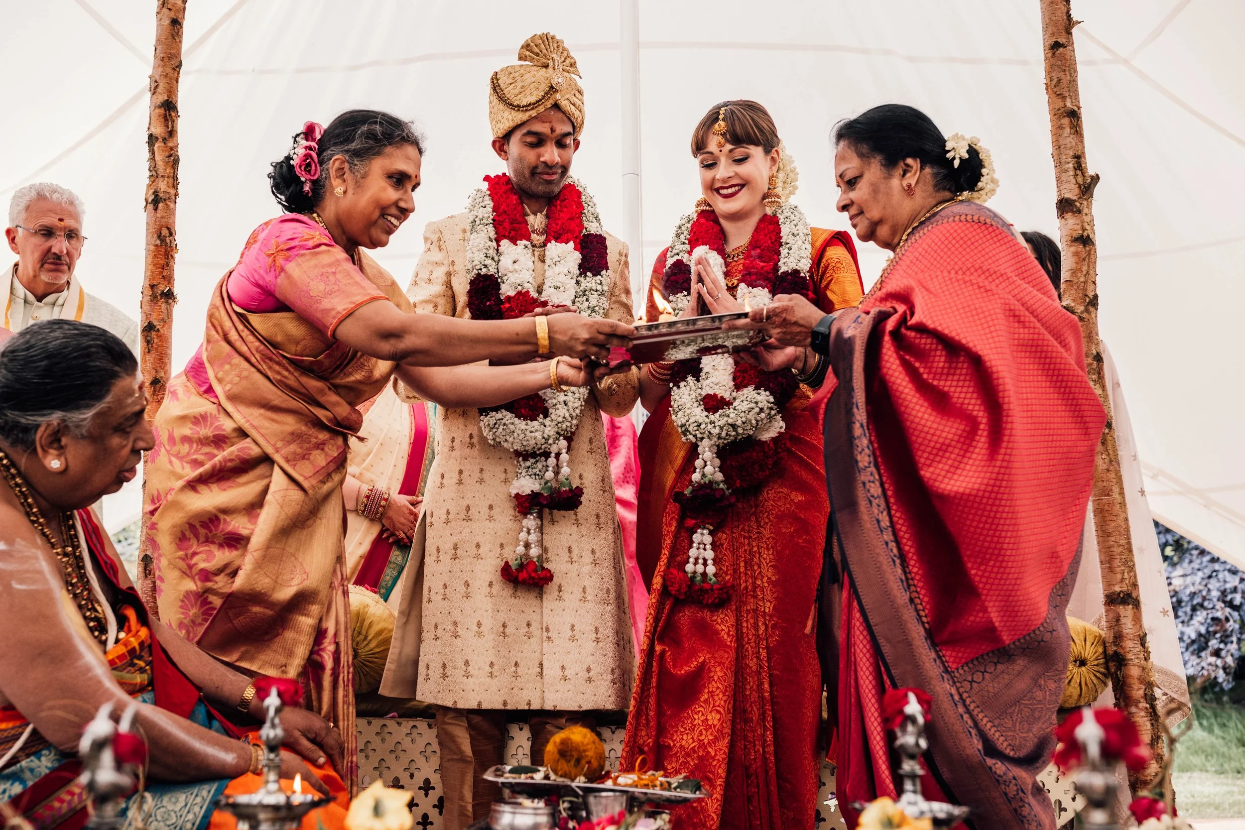 Indian wedding ceremony with bride and groom performing a traditional ritual under a canopy, surrounded by family members.