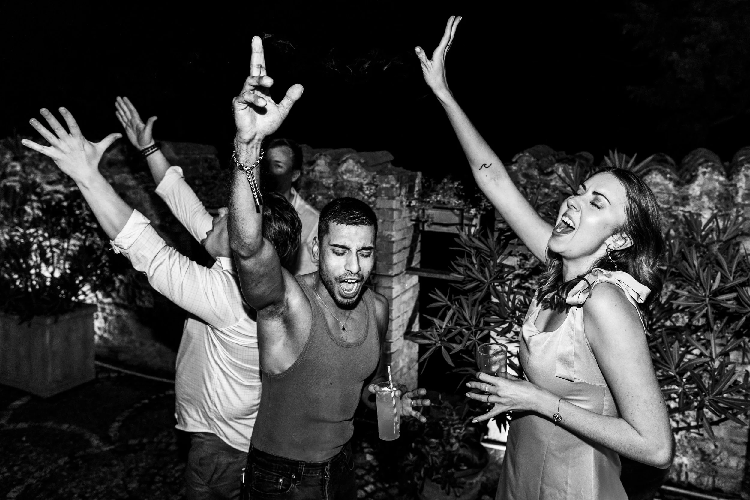 Group of young adults dancing, singing, and enjoying drinks at a lively outdoor night party.
