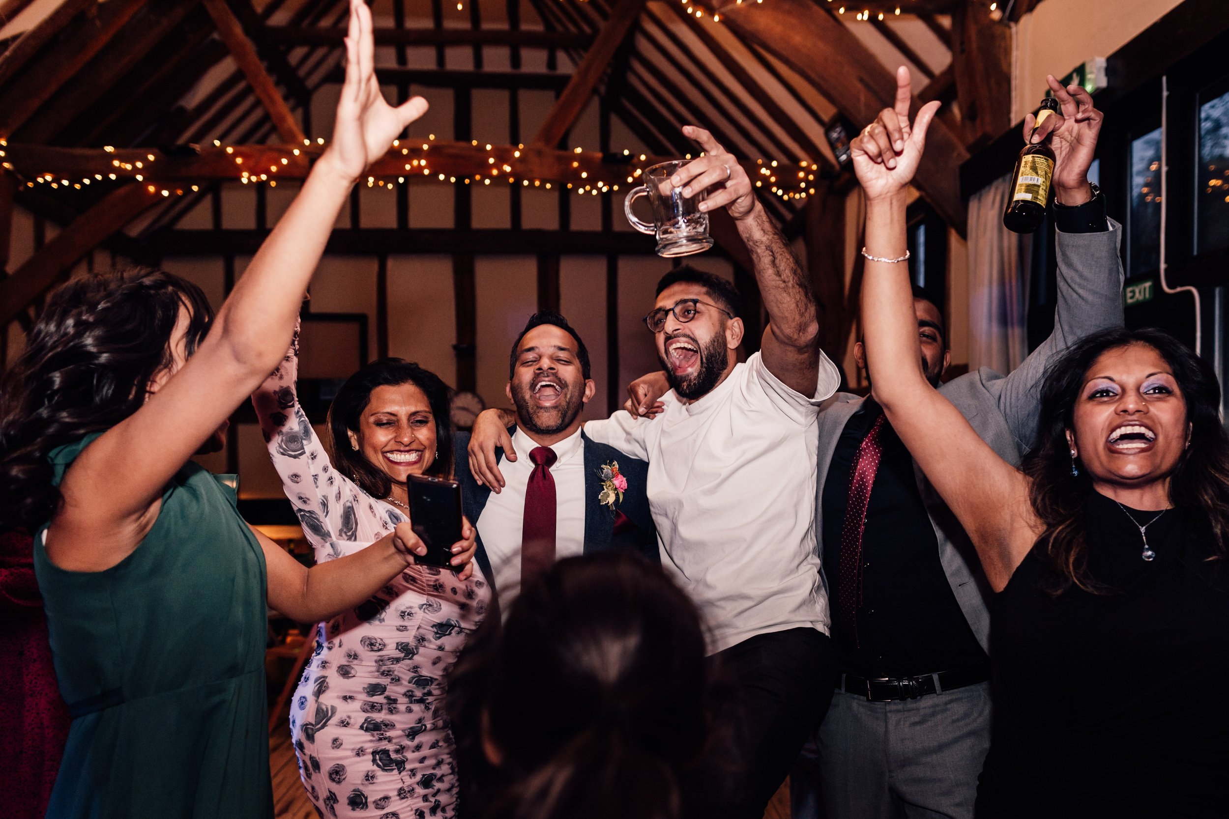 People celebrating and dancing at a party in a decorated indoor venue, smiling and raising their hands.