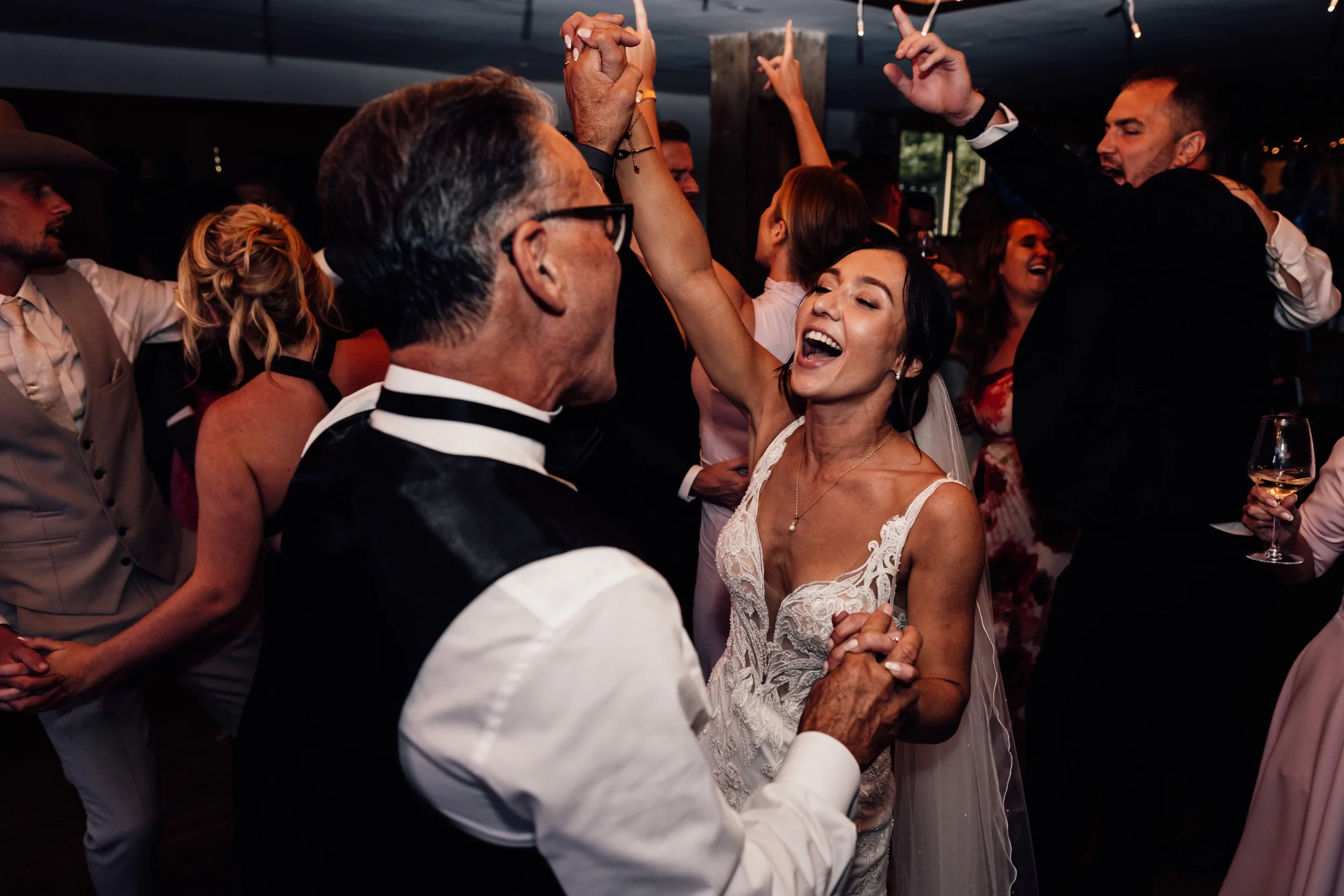 A bride and groom dancing with guests at a wedding reception, smiling and enjoying the celebration.