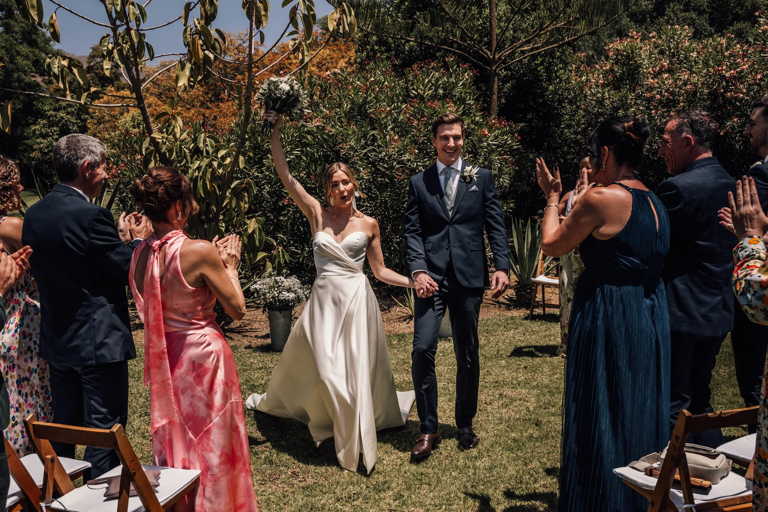 Bride & groom walking towards camera cheering after wedding ceremony in hot country