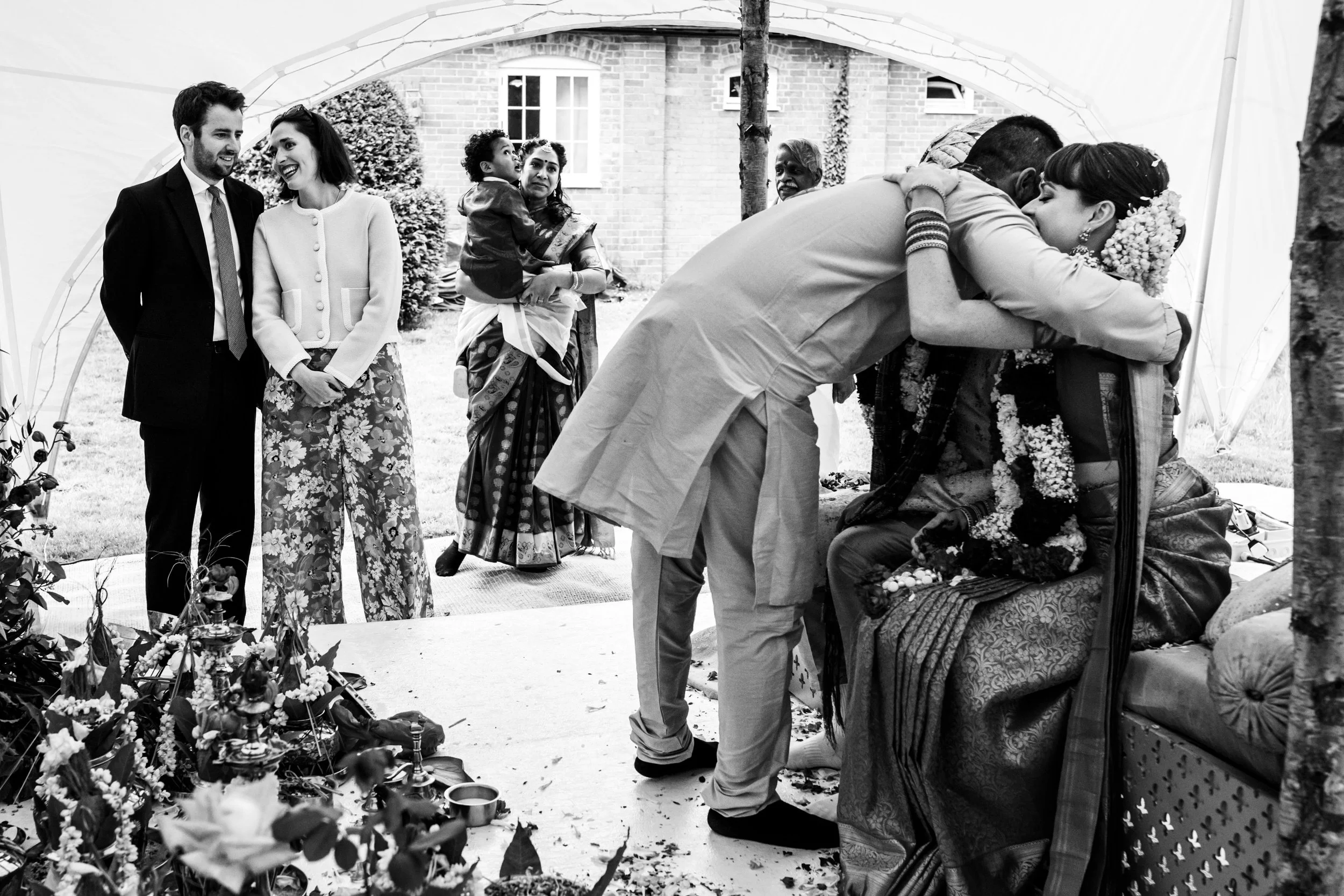People participating in a traditional wedding ceremony outdoors, with a couple embracing and others observing.