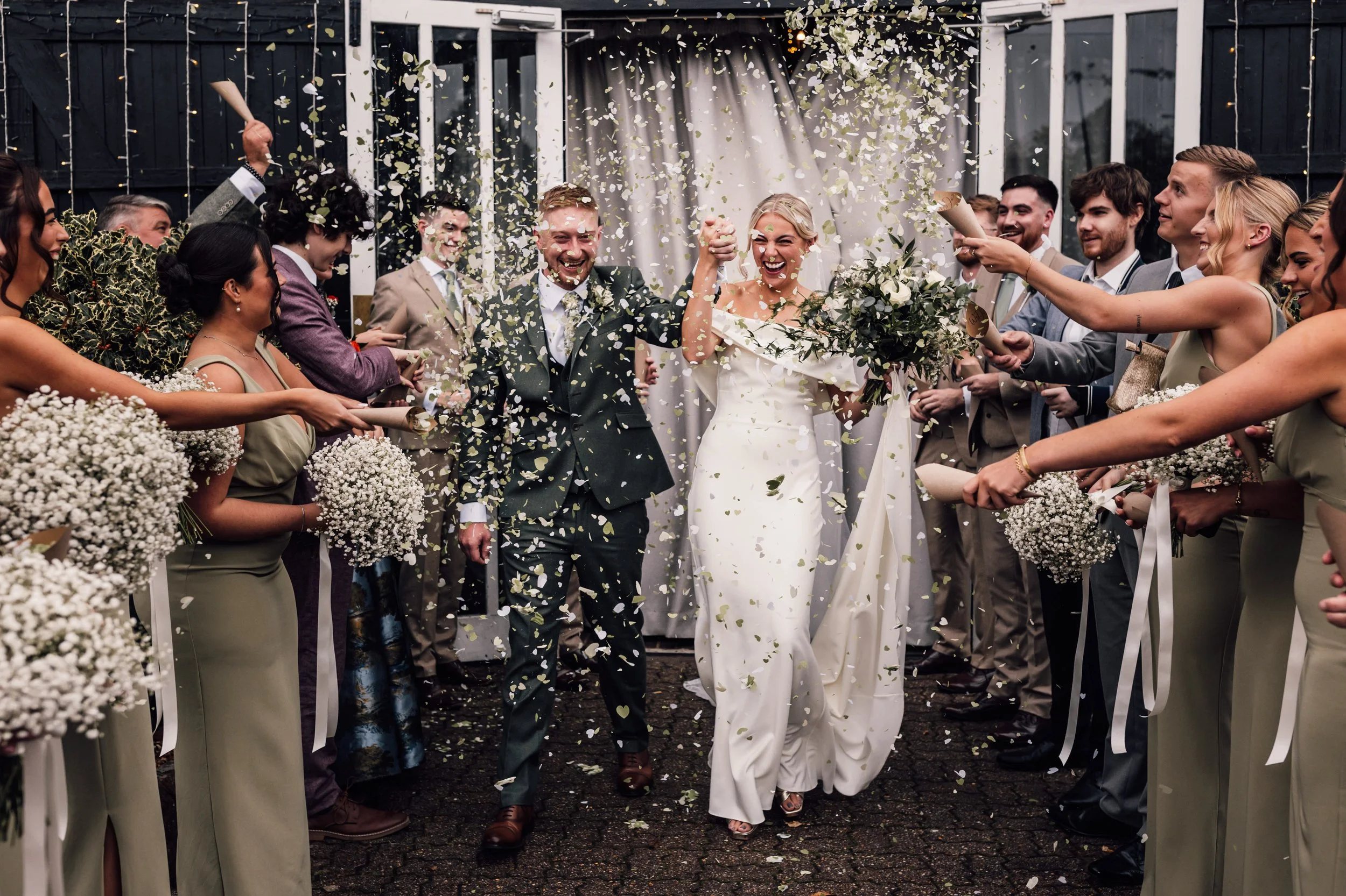 Bride and groom walking through a celebration with friends and family, confetti falling, during wedding