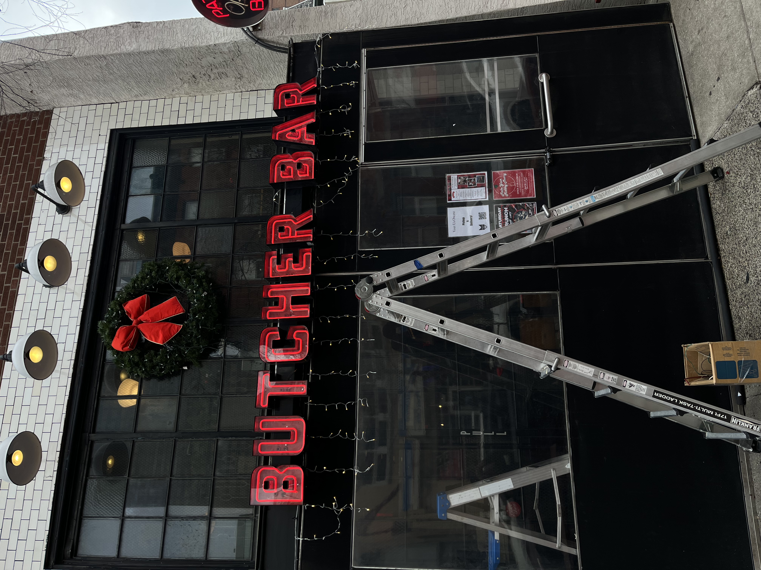 Red neon sign spelling 'BUTCHER BAR' mounted on the exterior wall of a restaurant. 