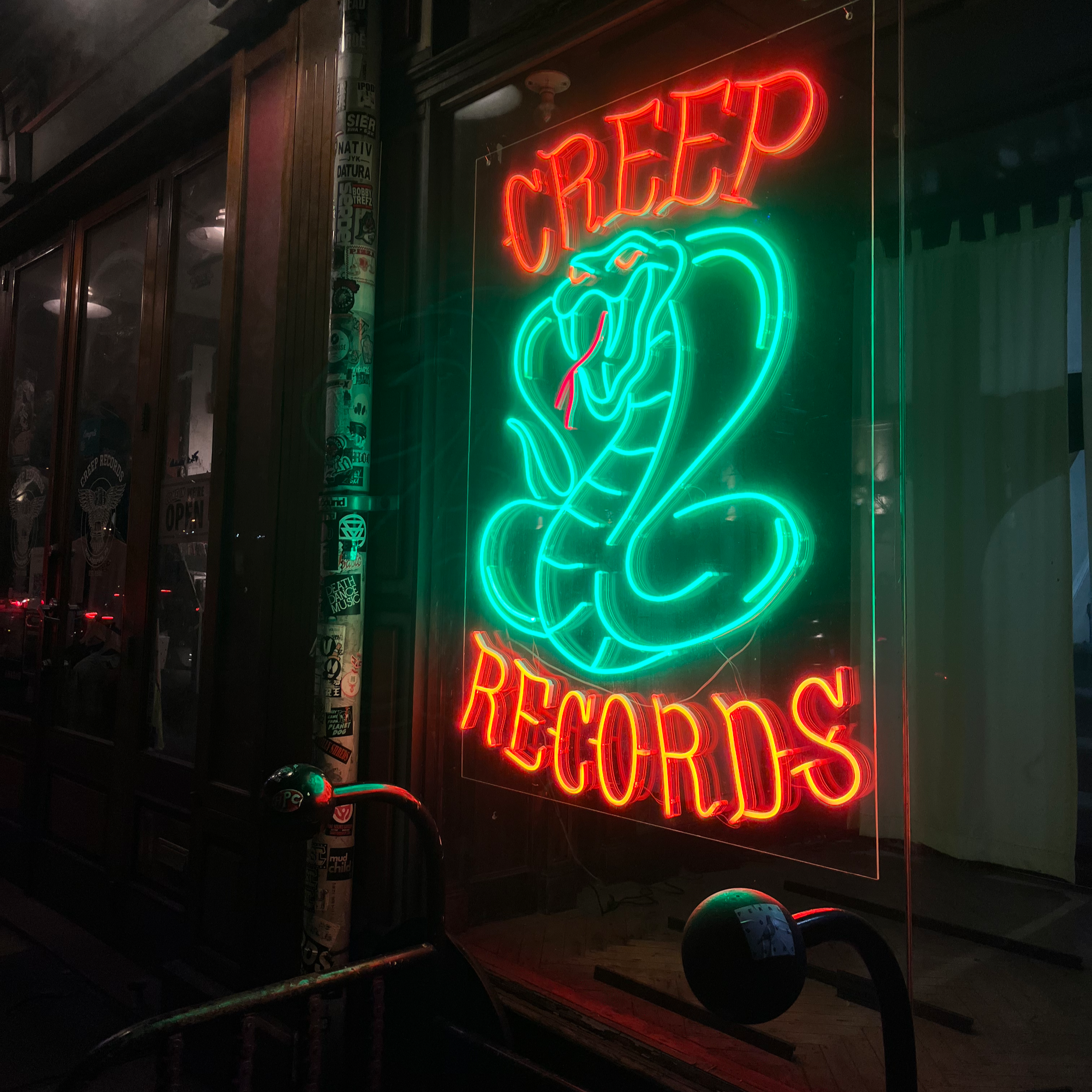 Neon sign reading 'CREEP' and 'RECORDS' featuring a snake or design, displayed in a dark storefront window.