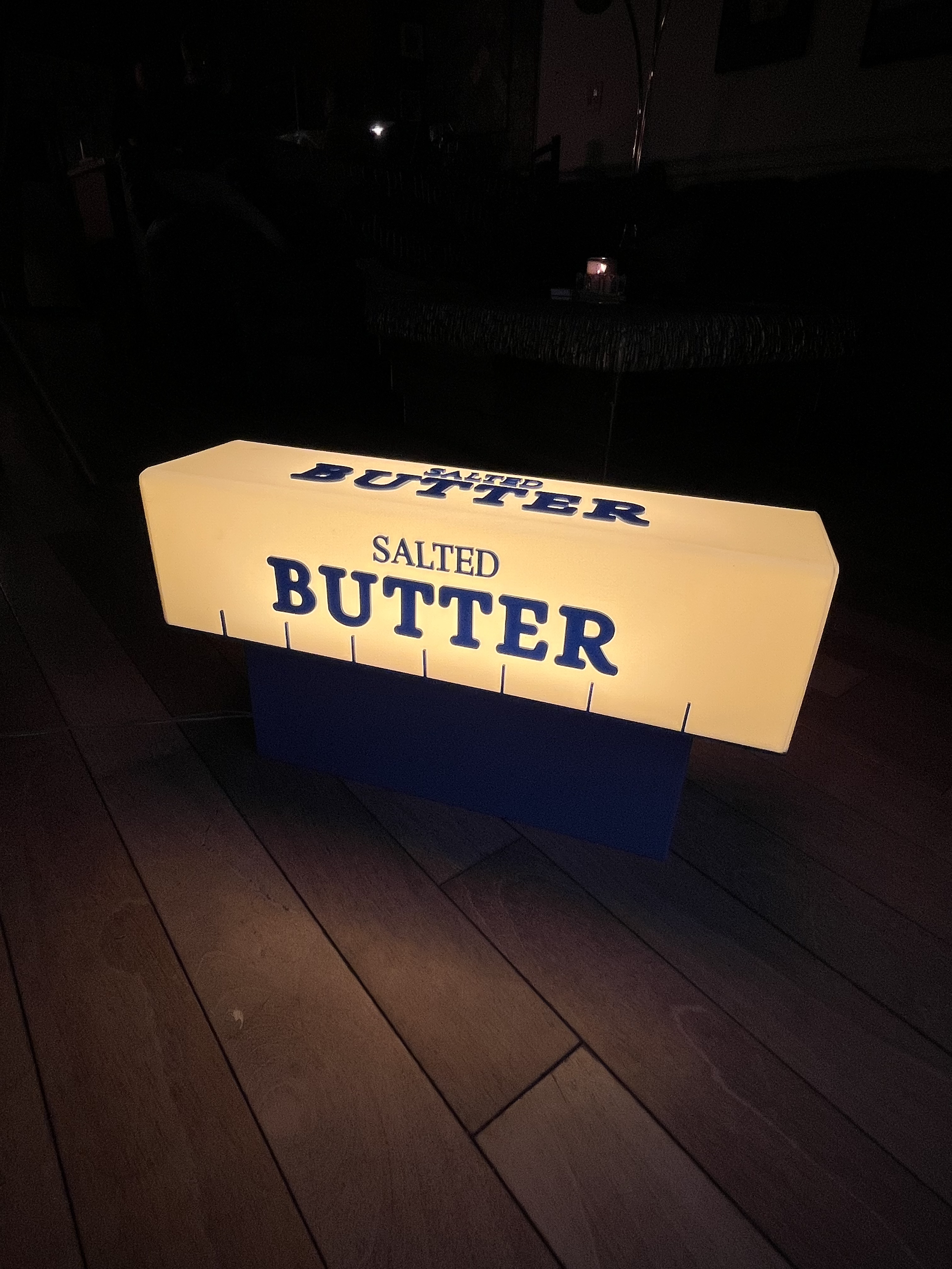 A Lightbox sign displaying the words 'Salted Butter' on a dark background, placed on a wooden surface.