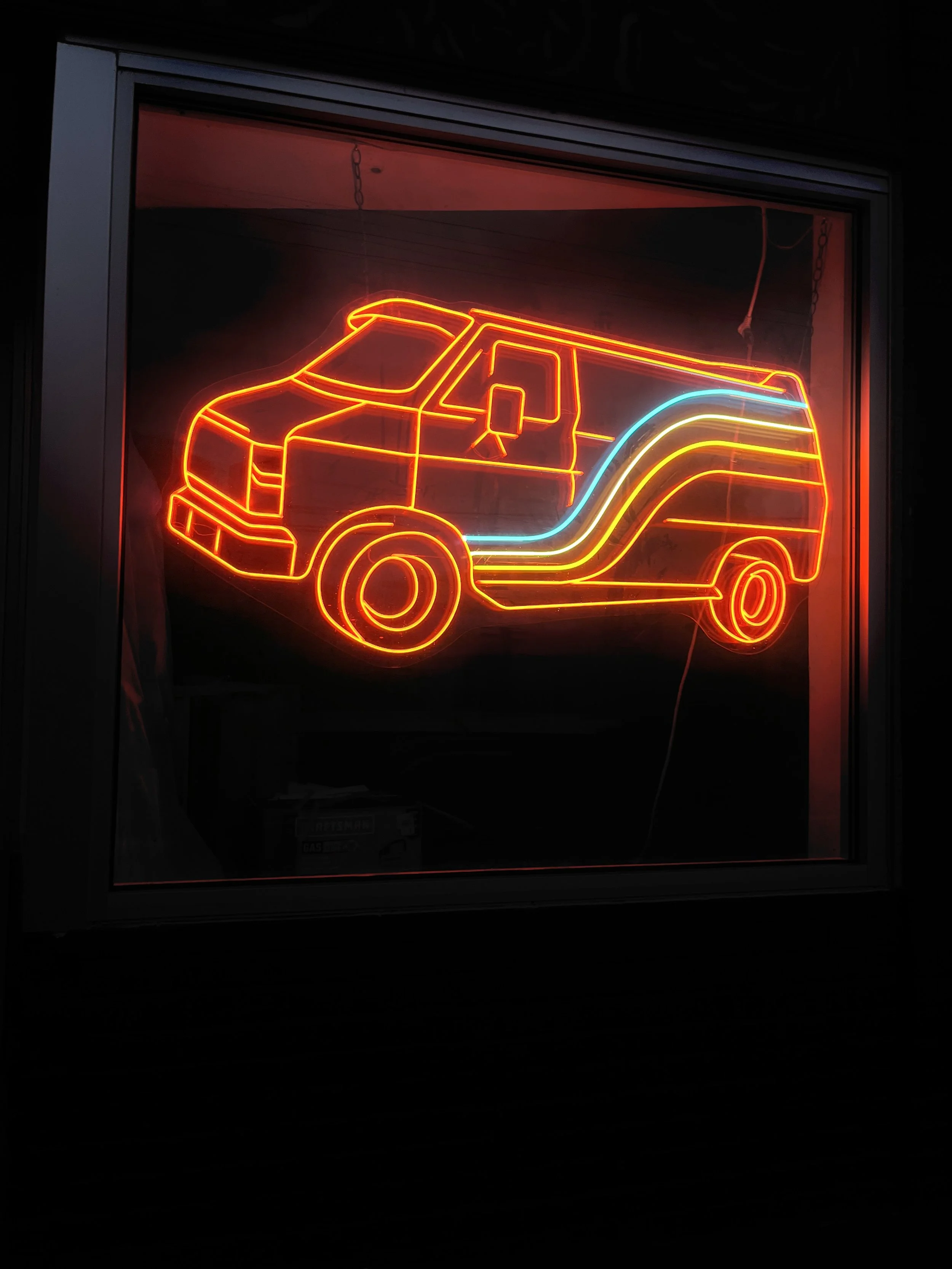 Neon sign of a van with blue, yellow, and red lines, displayed inside a window.